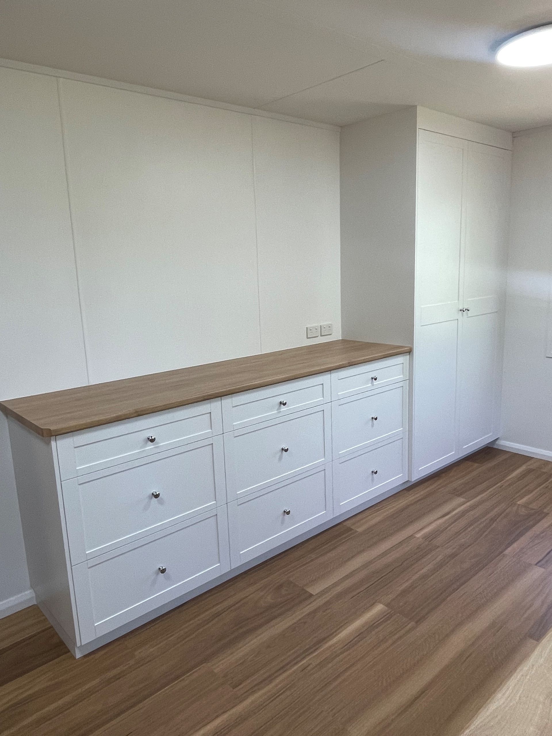 White dresser with wooden top against a wall in a mostly empty room with hardwood floors. — Valley Cabinetmakers In Biloela, QLD 