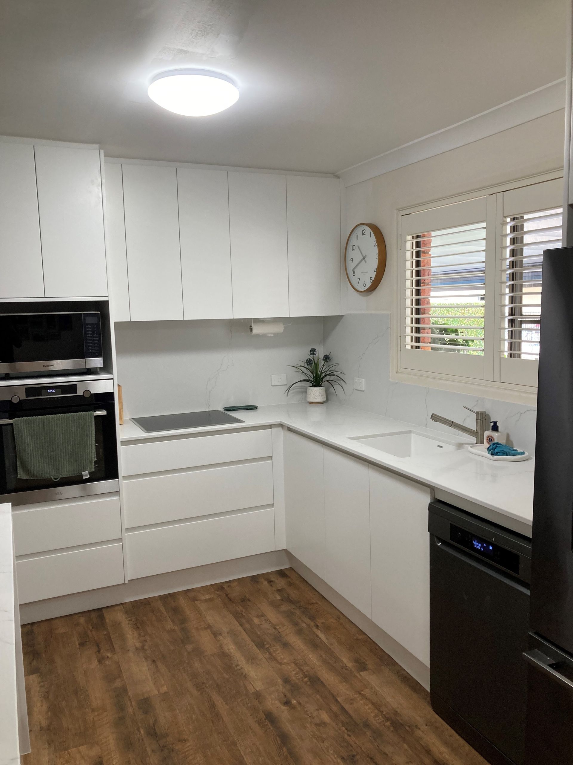 Modern white kitchen with black appliances, wood floor, window, and countertop sink — Valley Cabinetmakers In Biloela, QLD 
