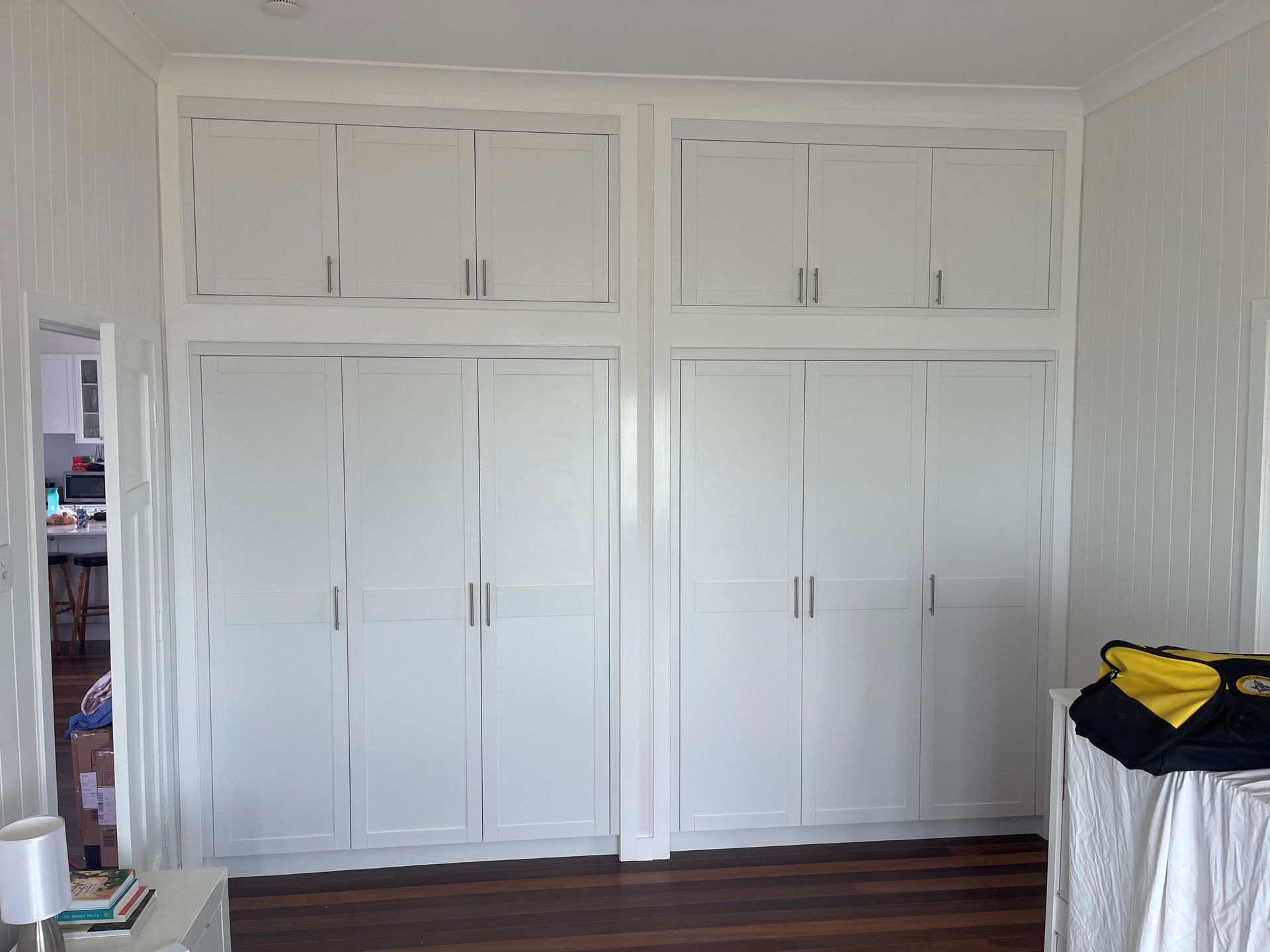 White built-in closet doors with upper cabinets in a bright bedroom, with a small table at right.— Valley Cabinetmakers In Biloela, QLD 