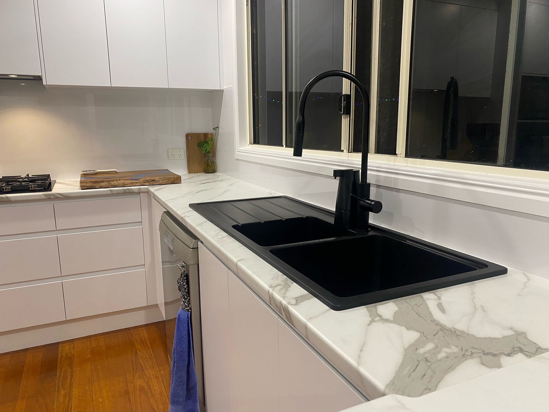 Modern kitchen sink with black faucet, white cabinets, marble countertop, and window view at night — Valley Cabinetmakers In Biloela, QLD 
