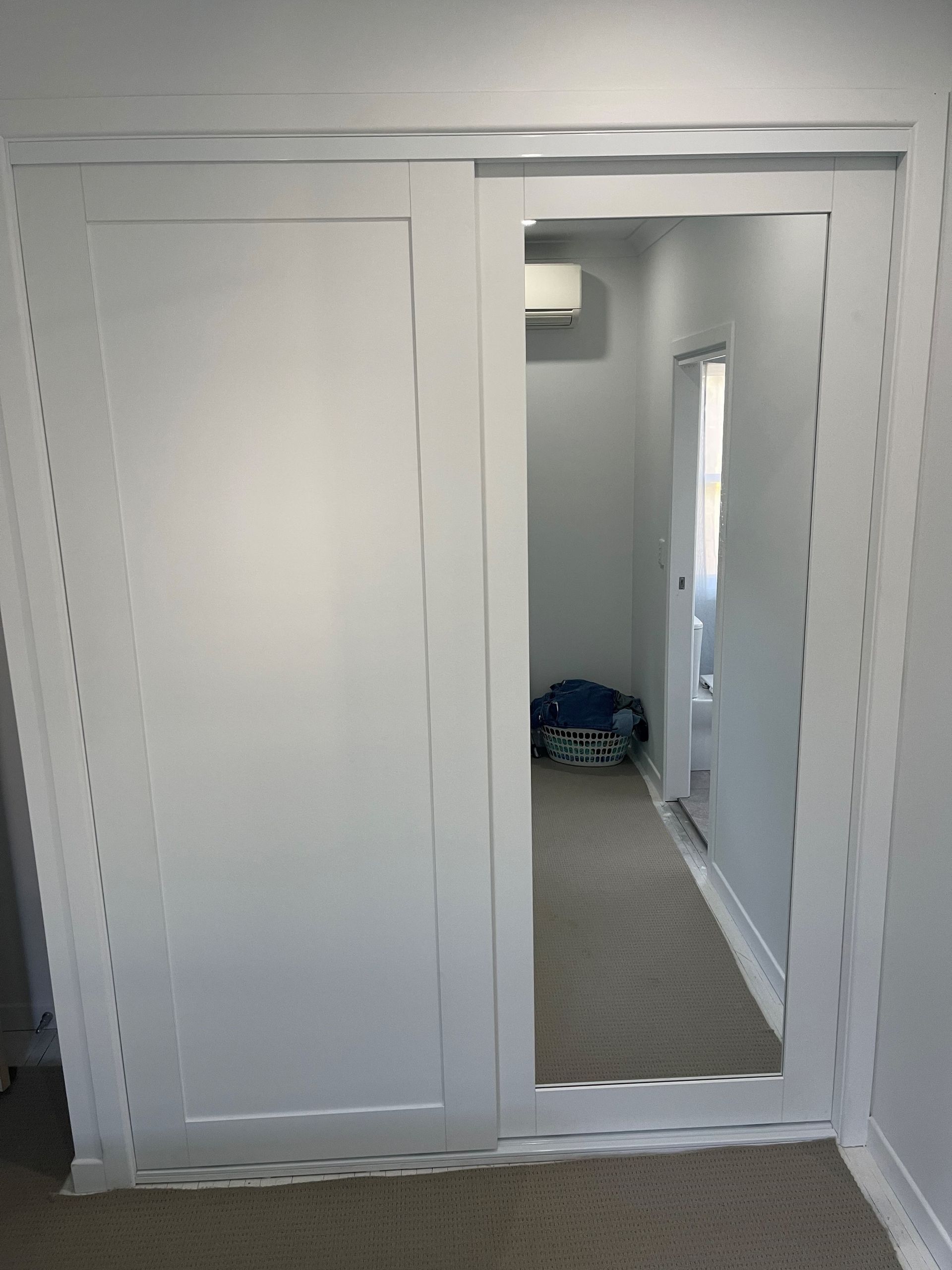 White closet doors, one closed and one mirrored open, showing a hallway and carpet inside. — Valley Cabinetmakers In Biloela, QLD 