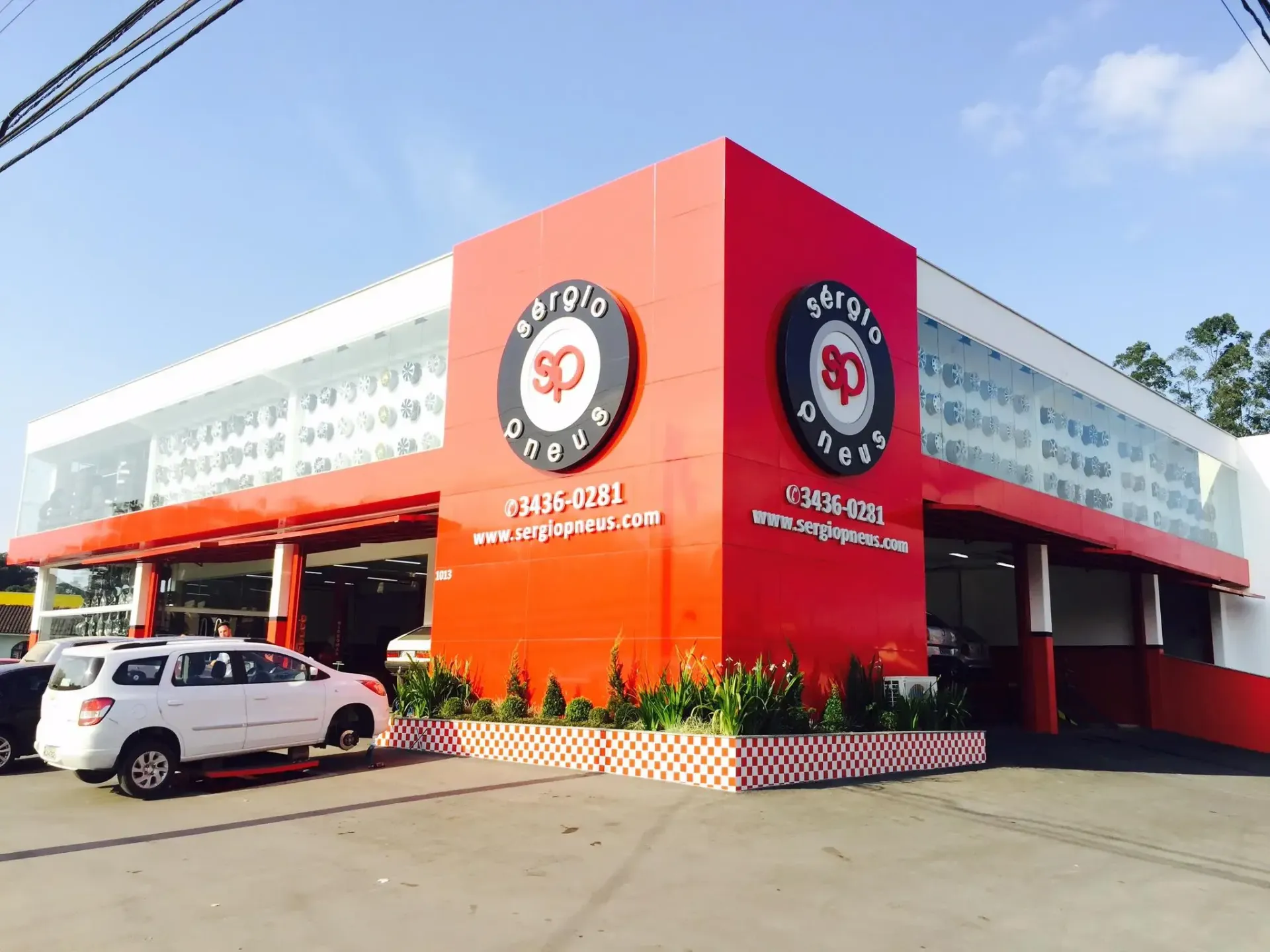 Prédio de serviço automotivo vermelho brilhante com placas com o logotipo, carros estacionados e uma entrada para veículos.