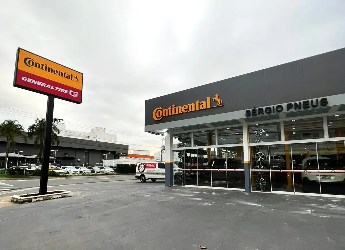 Fachada da loja de pneus Continental com placa laranja e entrada de vidro, vista do estacionamento.