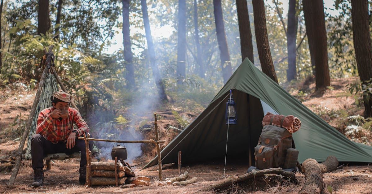 A man is sitting in front of a tent in the woods.