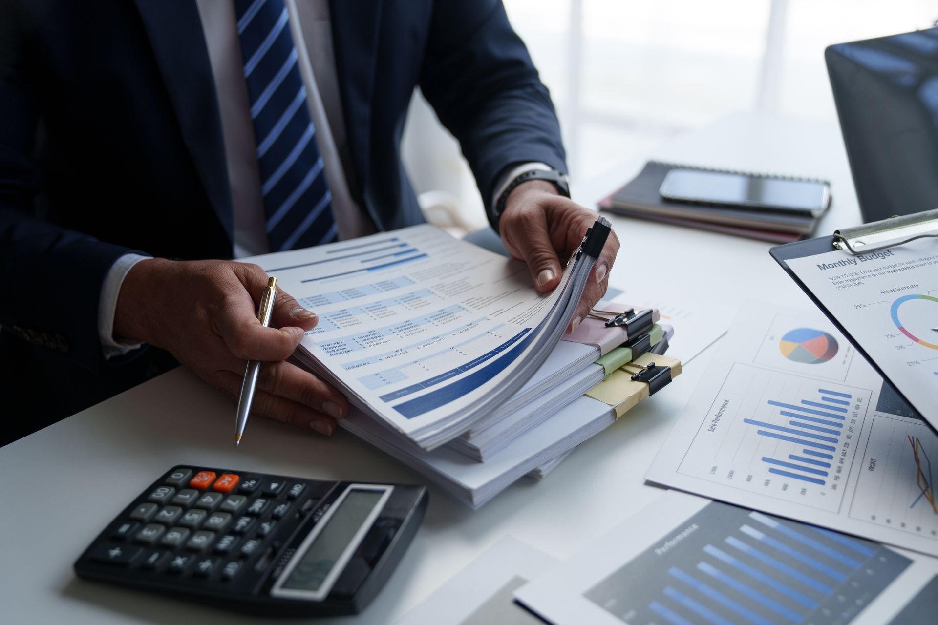 A man in a suit and tie is sitting at a desk with a calculator and papers.