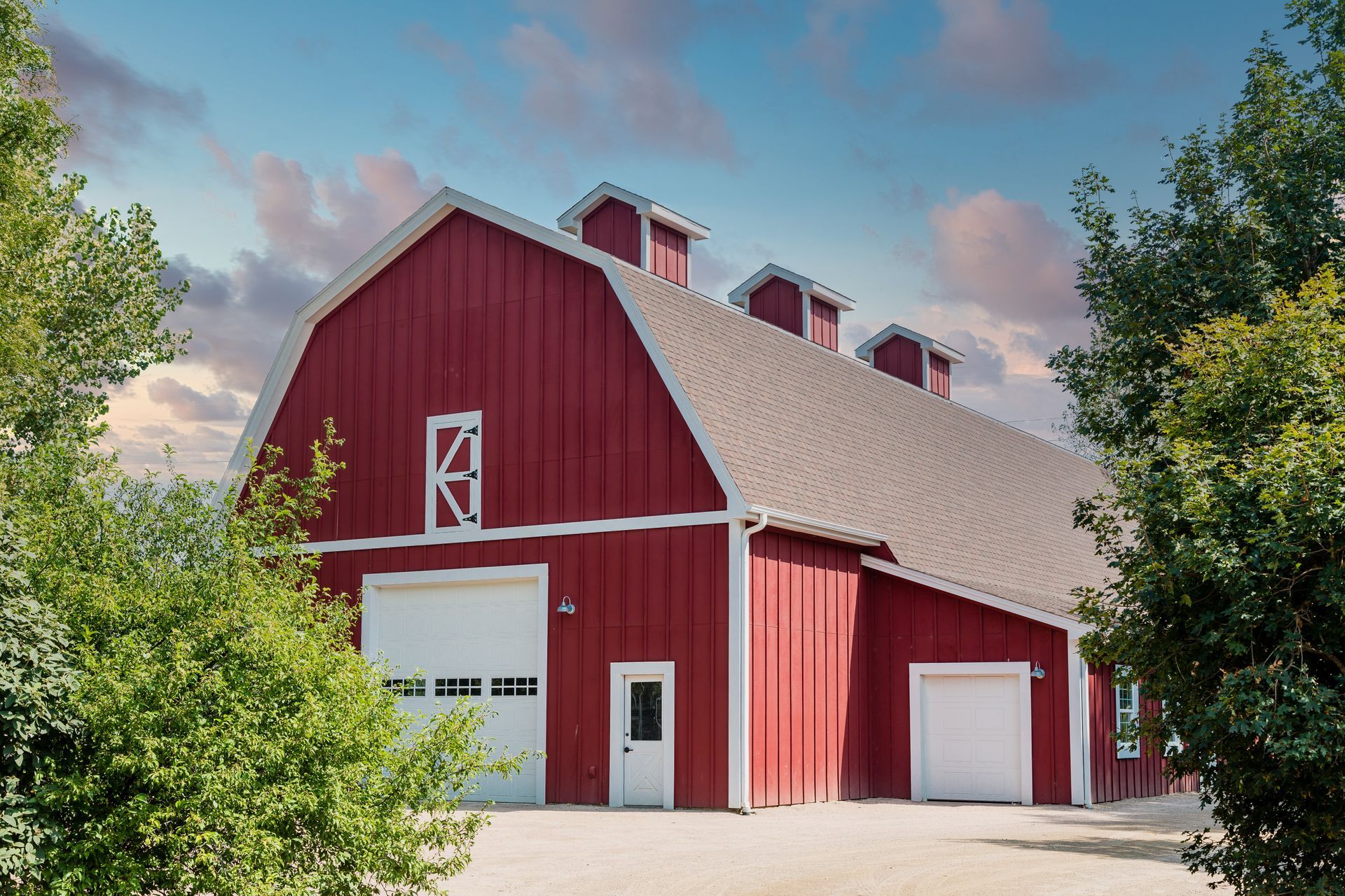 A large red barn with a white trim is surrounded by trees.