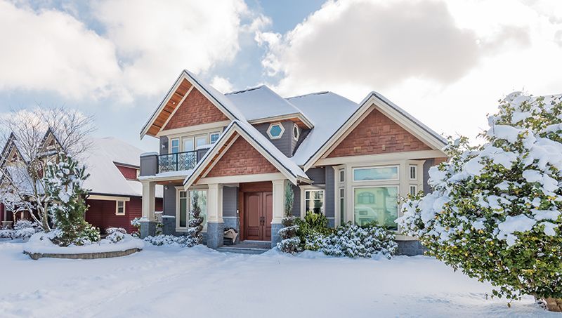 A large house is covered in snow on a sunny day.