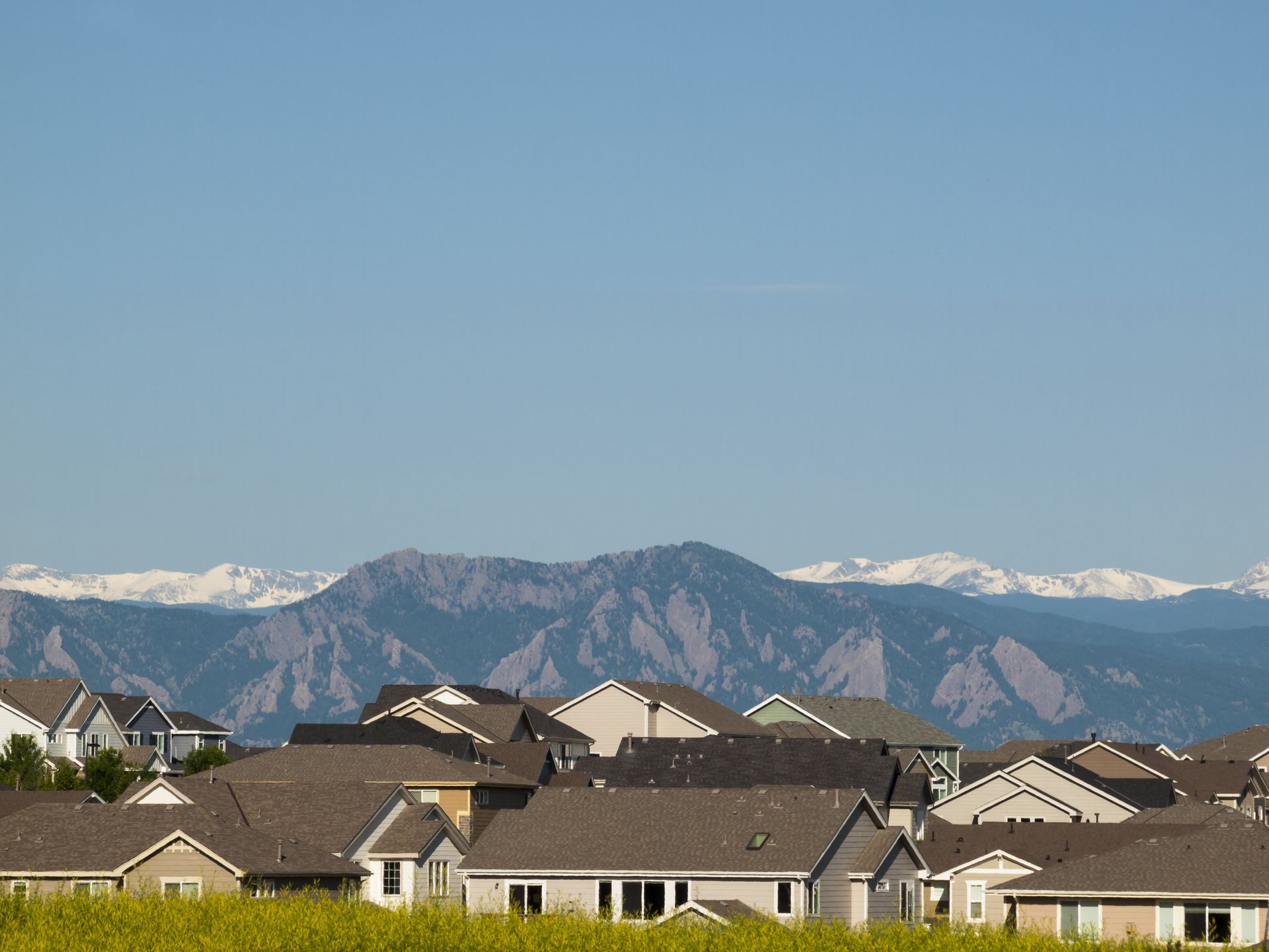 Houses with brown roofs against a backdrop of mountains under a clear blue sky.