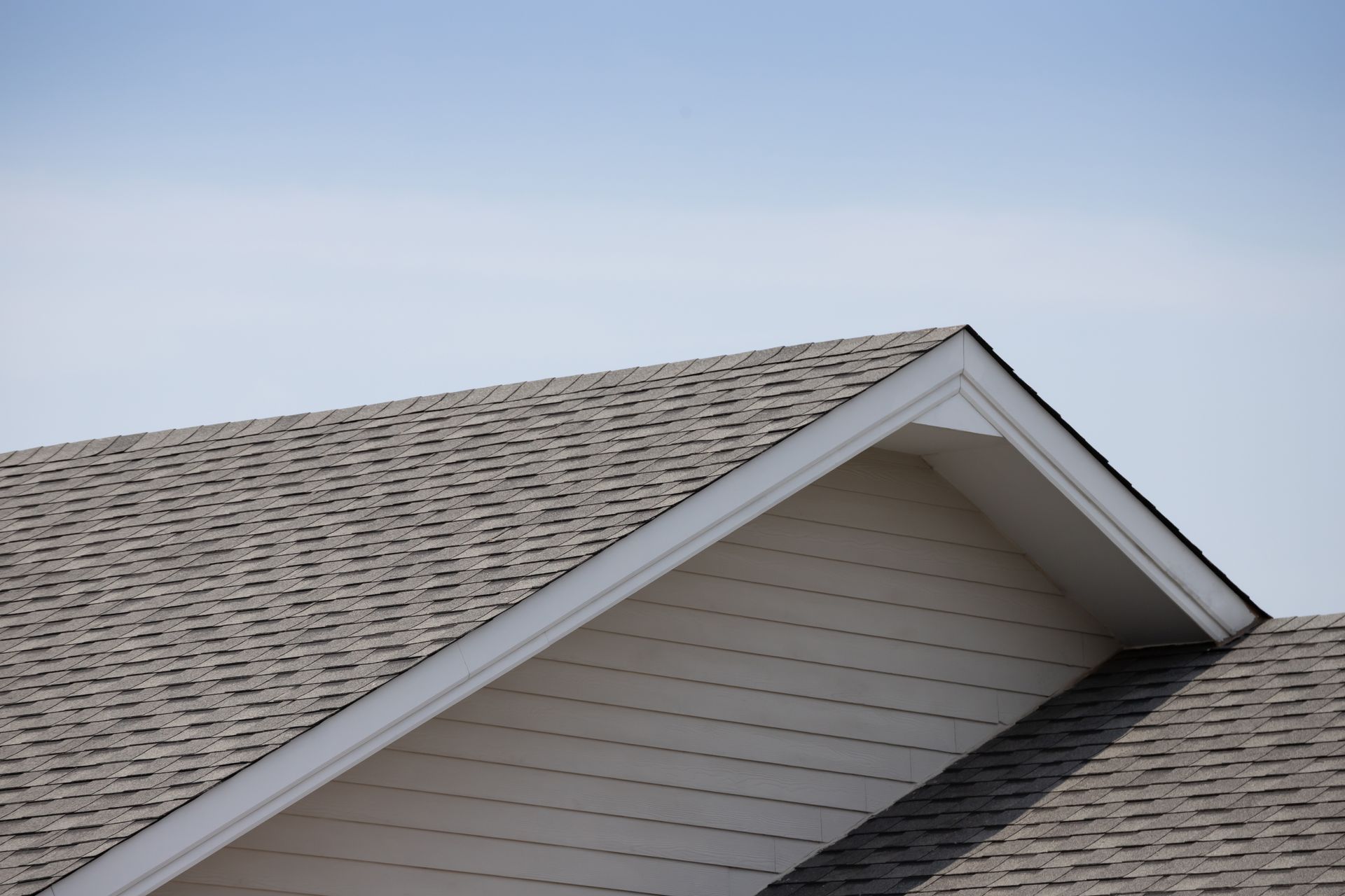 Roof of a house with gray shingles and white trim against a blue sky.
