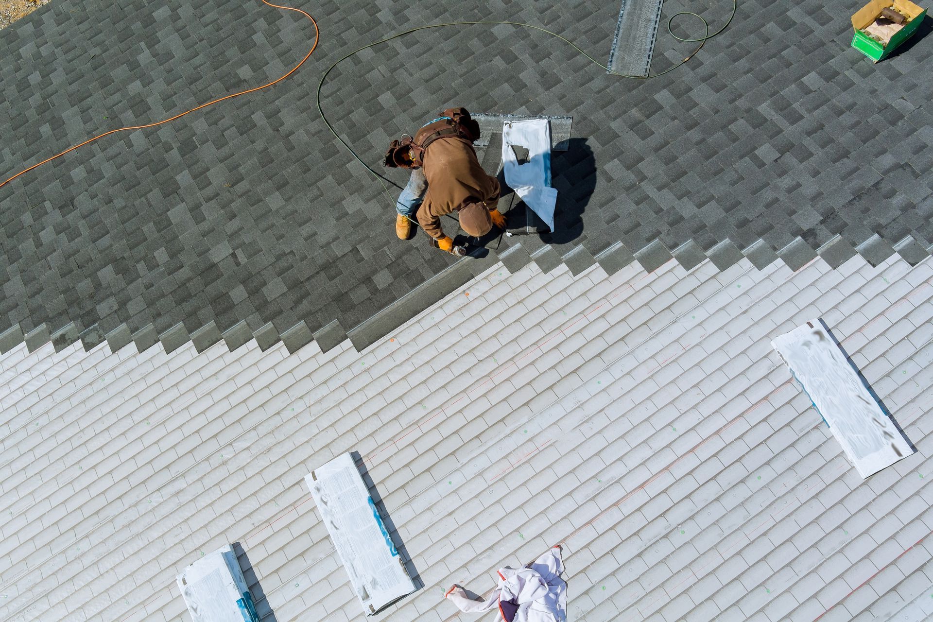 Roofer installing shingles on a house roof. Grey shingles contrast with light-colored underlayment.