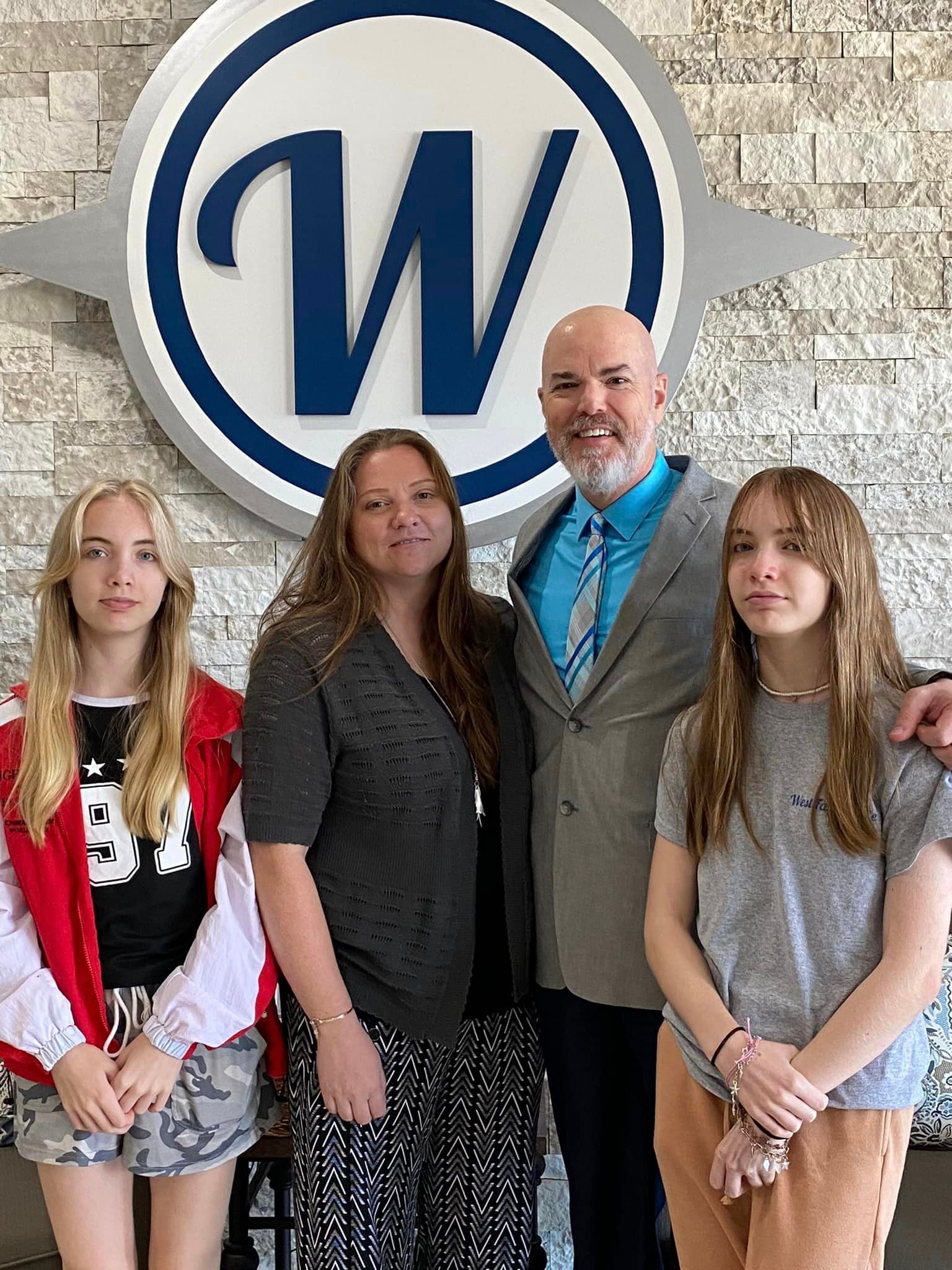 A man , woman , and two girls are posing for a picture in front of a sign.