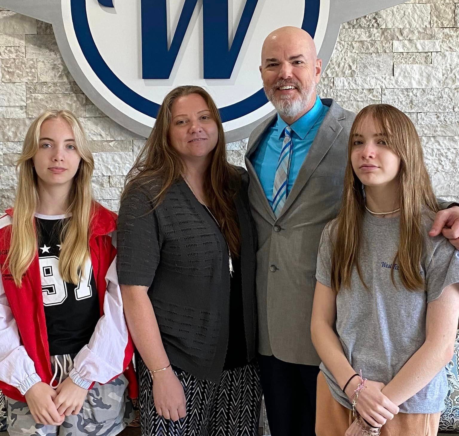 Family of four smiling, posing in front of a business logo with a man in a suit.