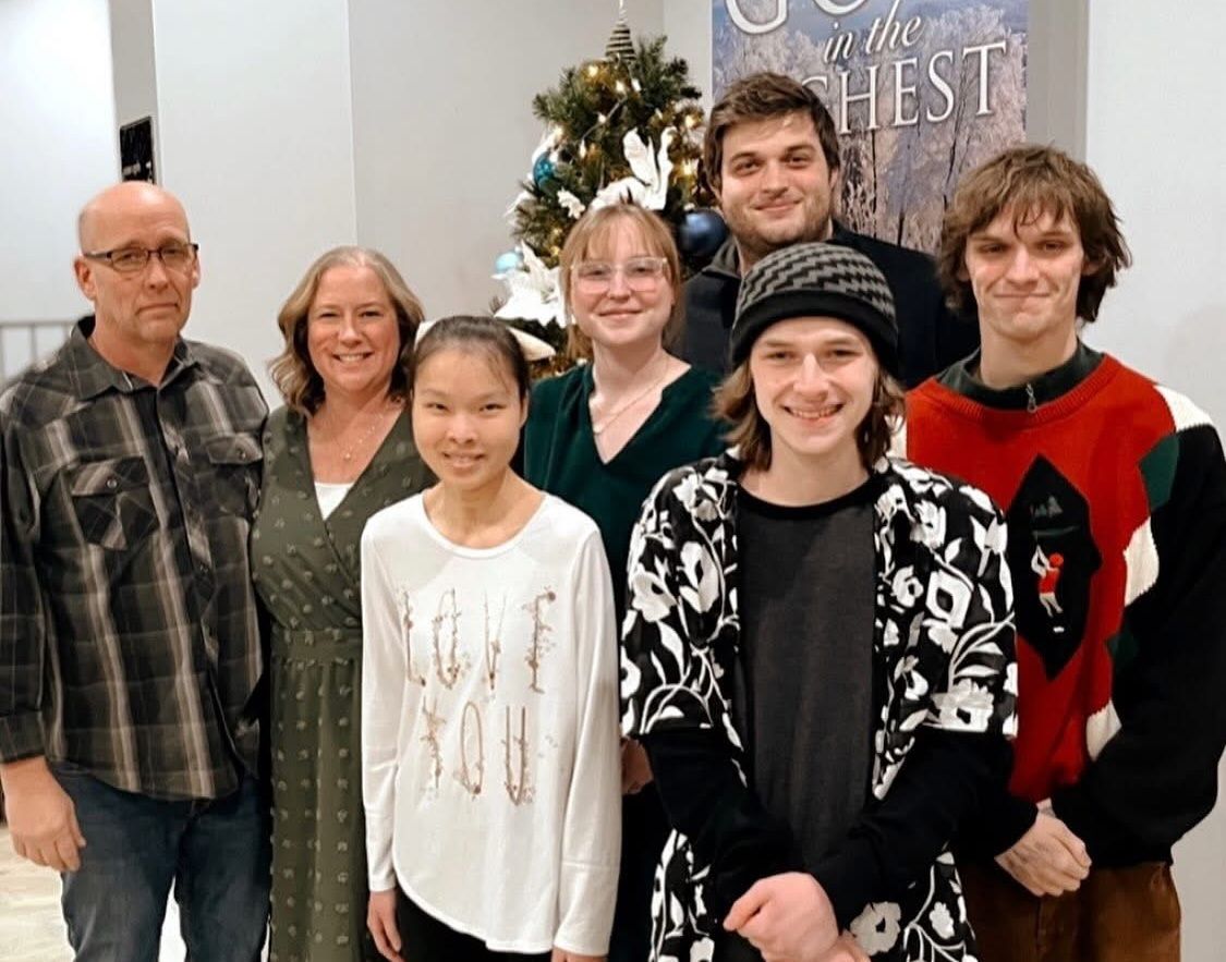 Family group posing in front of a Christmas tree. Adults and teens smiling.