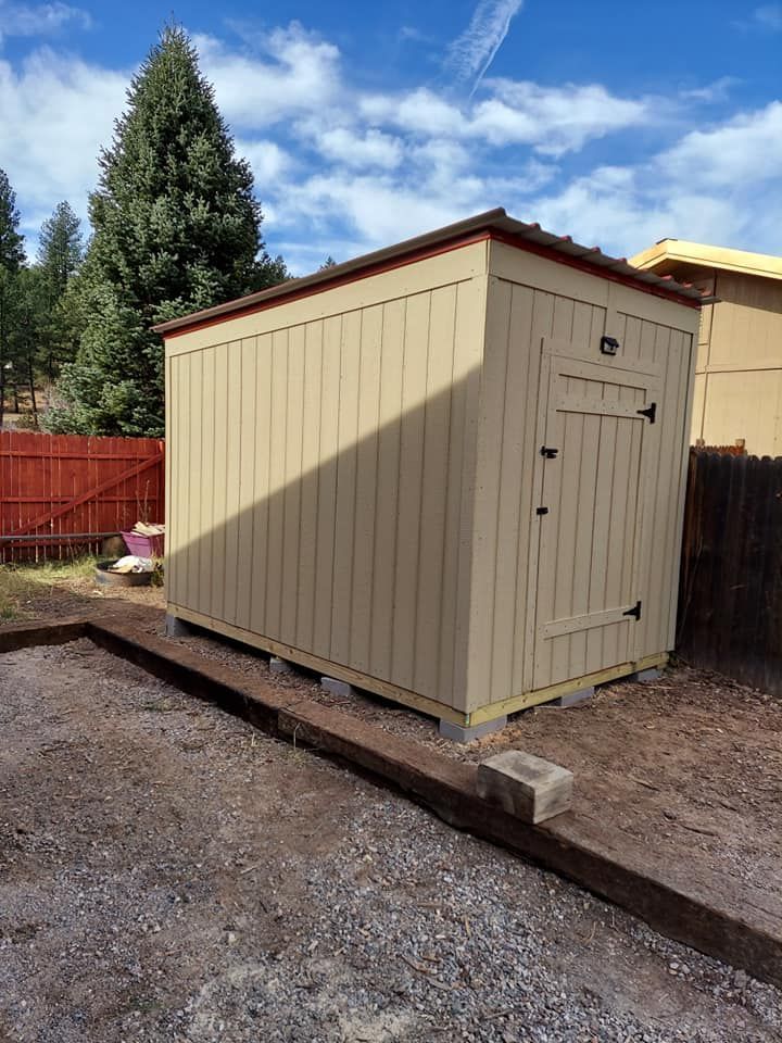 A small shed is sitting in the dirt in a backyard.
