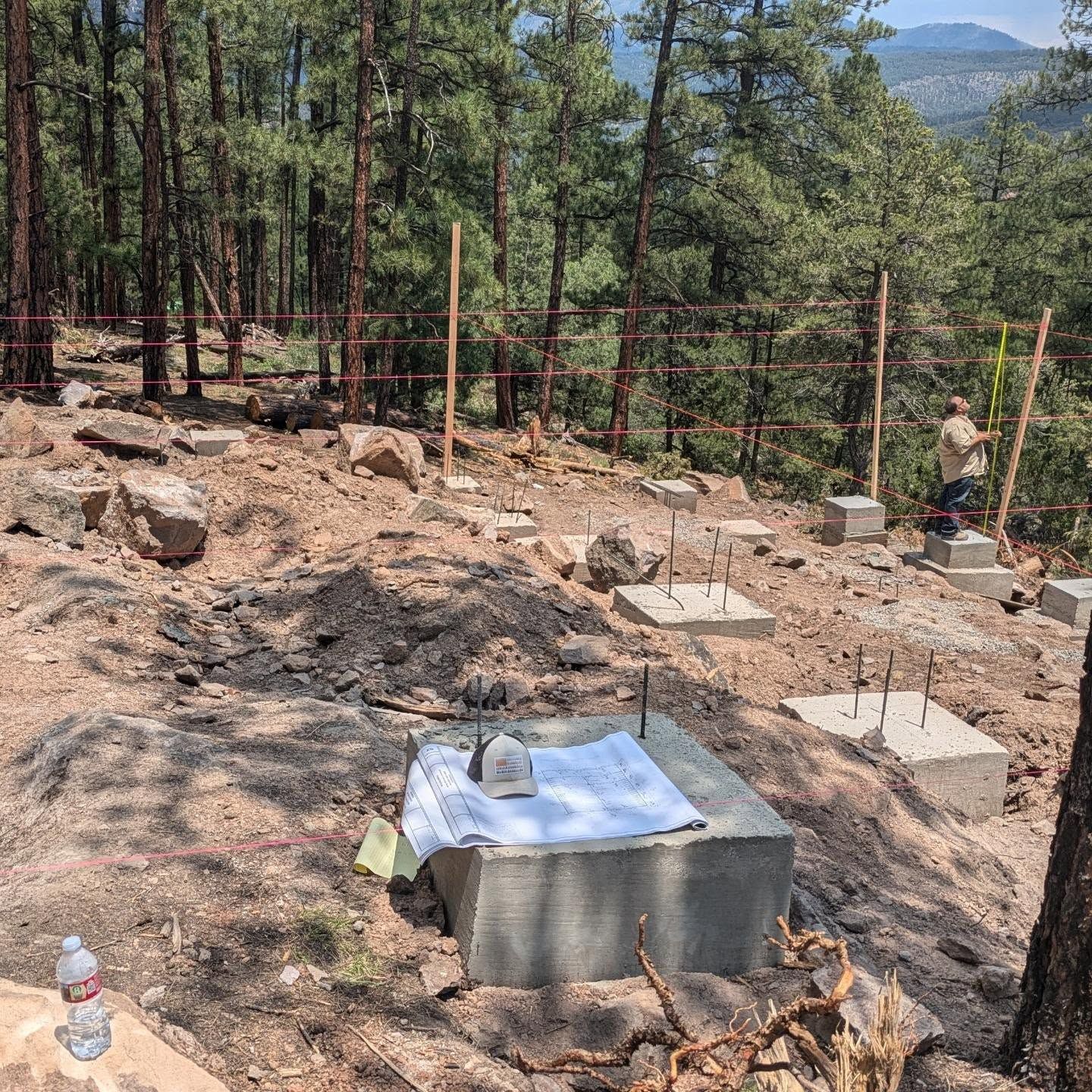 A construction site in the middle of a forest with a bottle of water in the foreground.