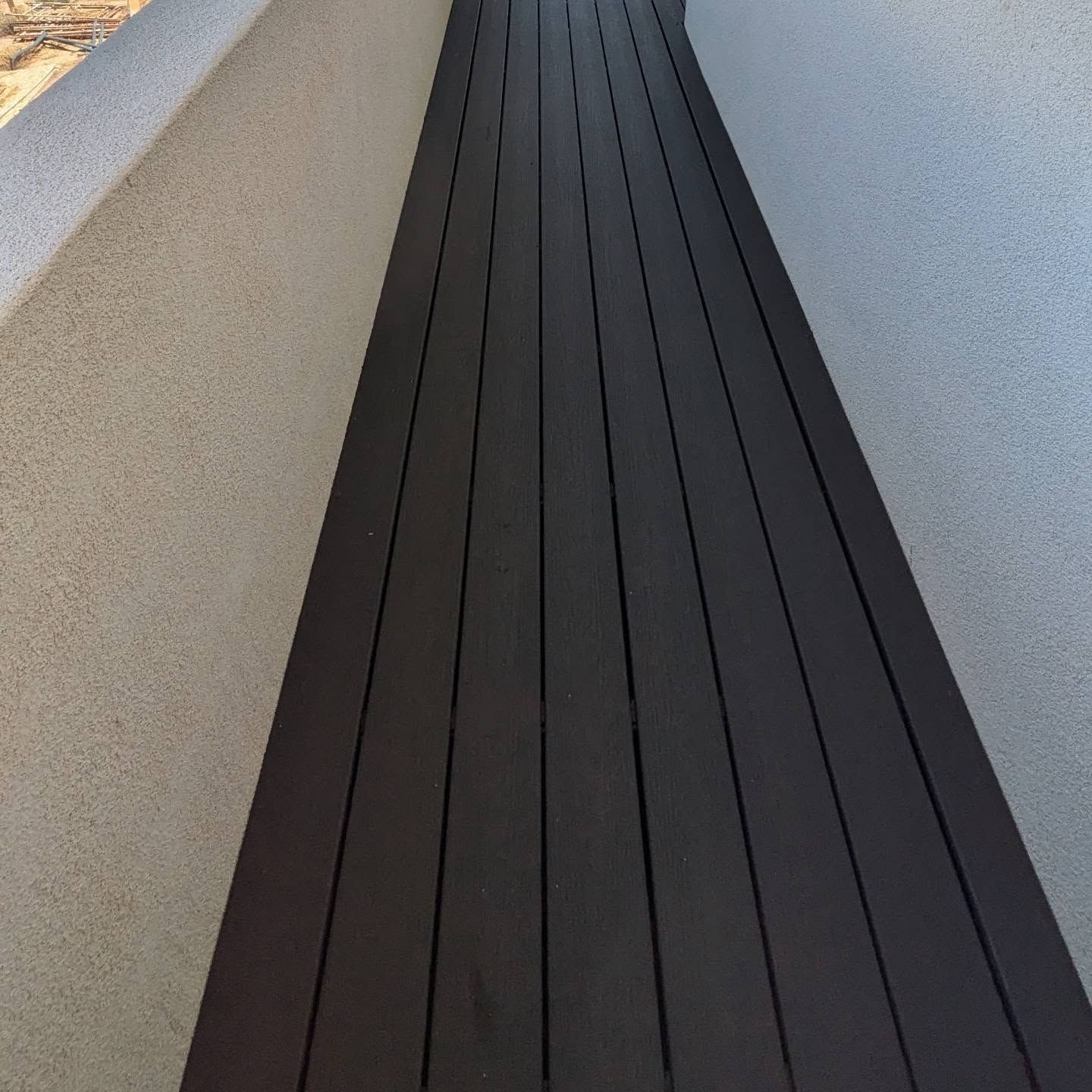 A wooden walkway with a white wall in the background