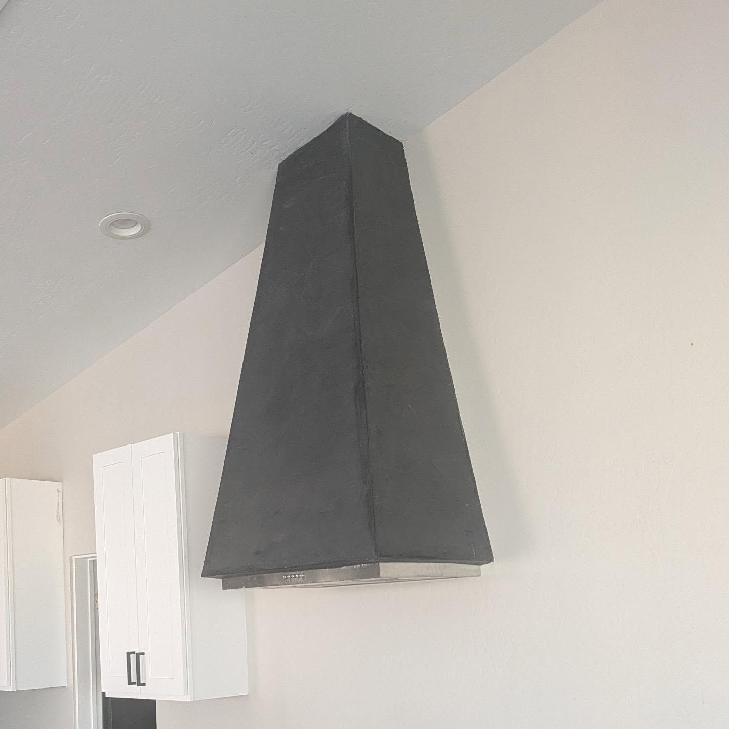 A black hood is hanging from the ceiling in a kitchen.