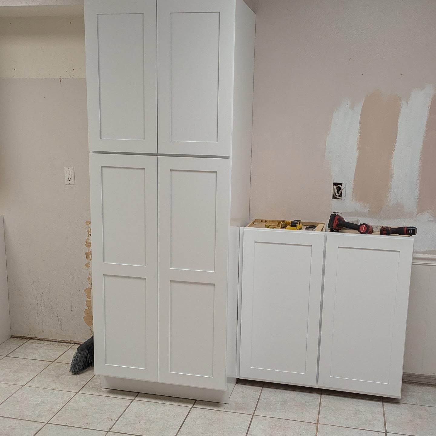 A room with white cabinets and a drill on the floor.