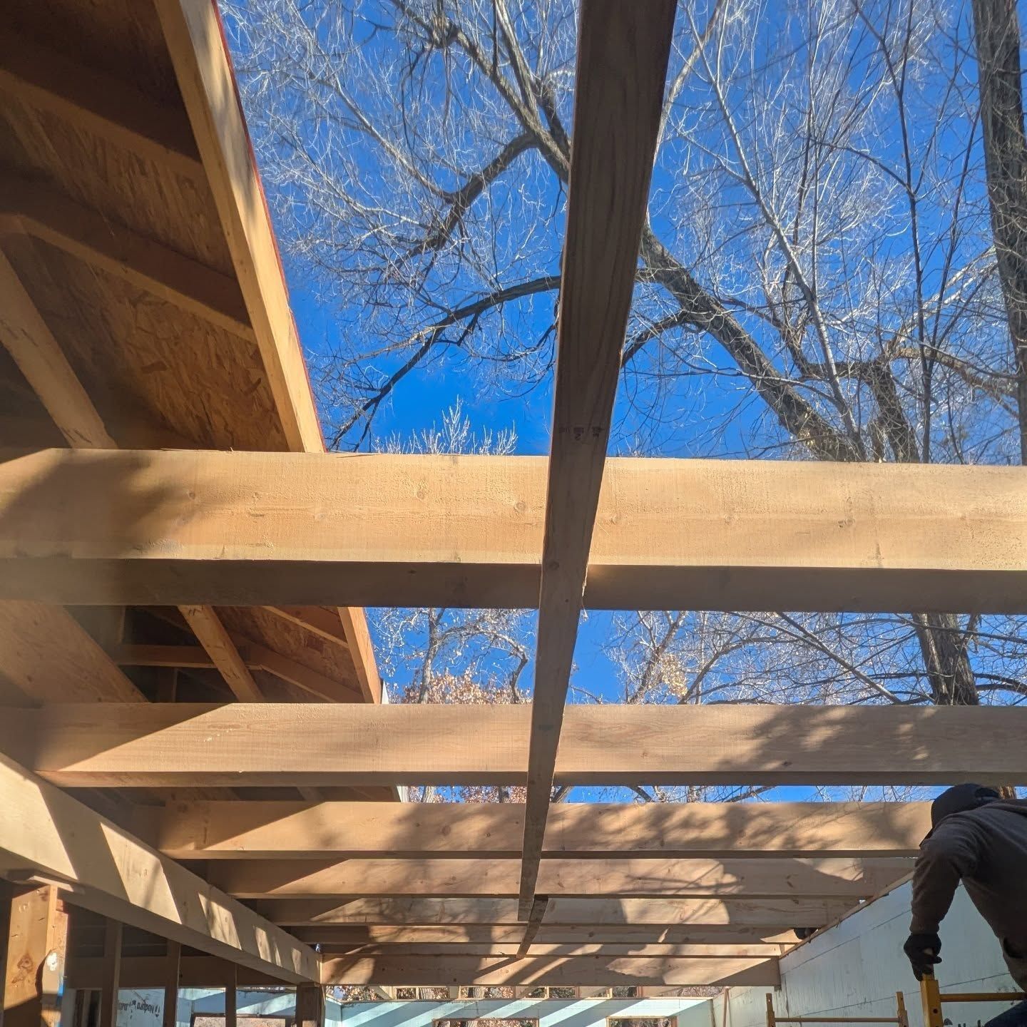 A man is working on a wooden structure with a blue sky in the background
