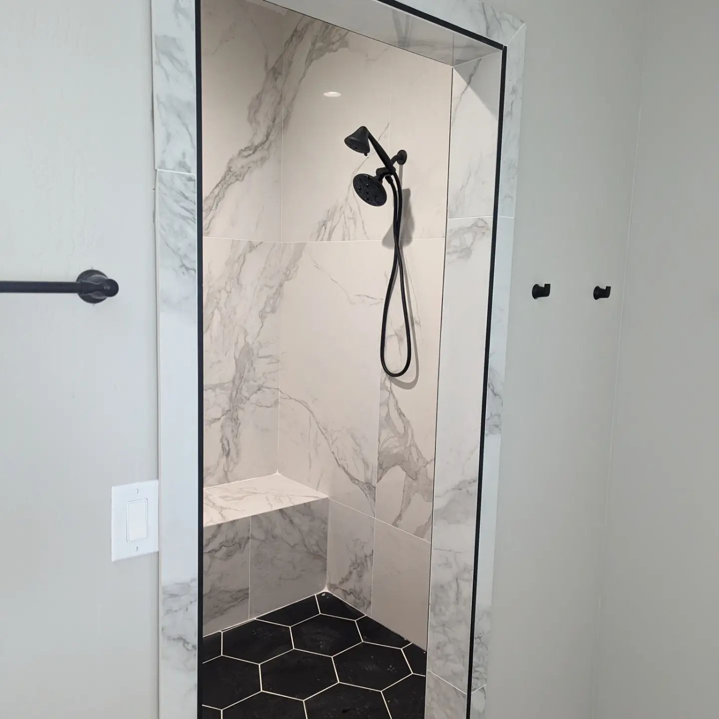 A bathroom with marble walls and a black shower head