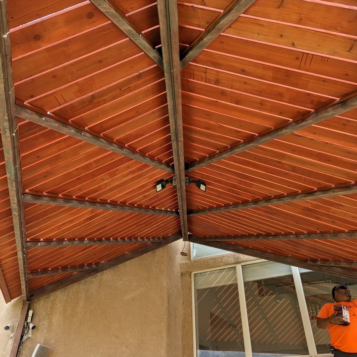 A man in an orange shirt is standing under a wooden roof