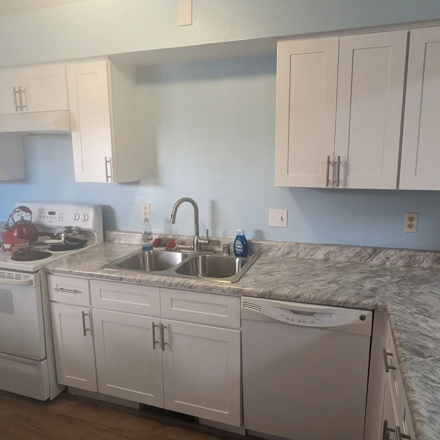 A kitchen with white cabinets , a sink , a stove , and a dishwasher.