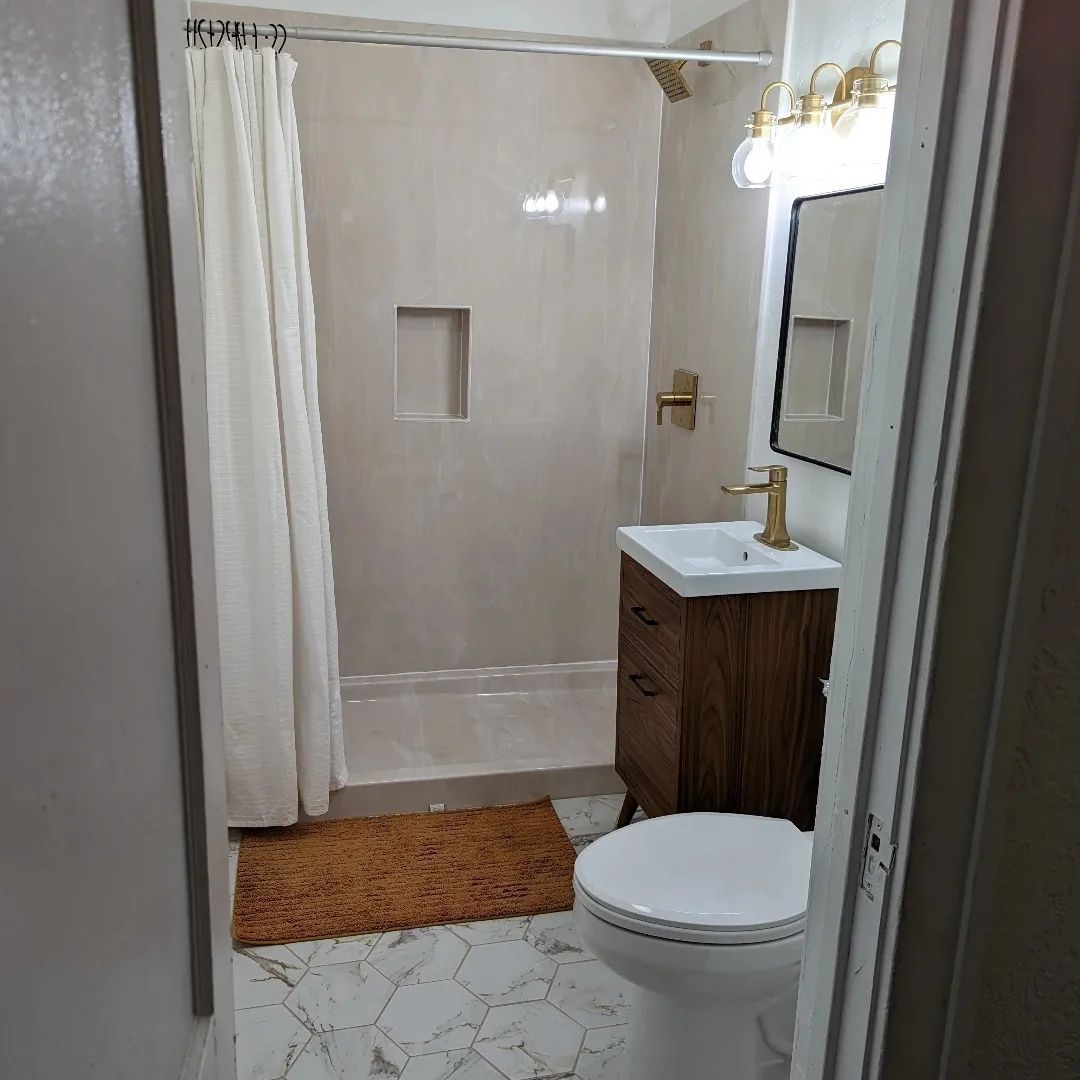 A bathroom with a toilet , sink , shower and mirror.
