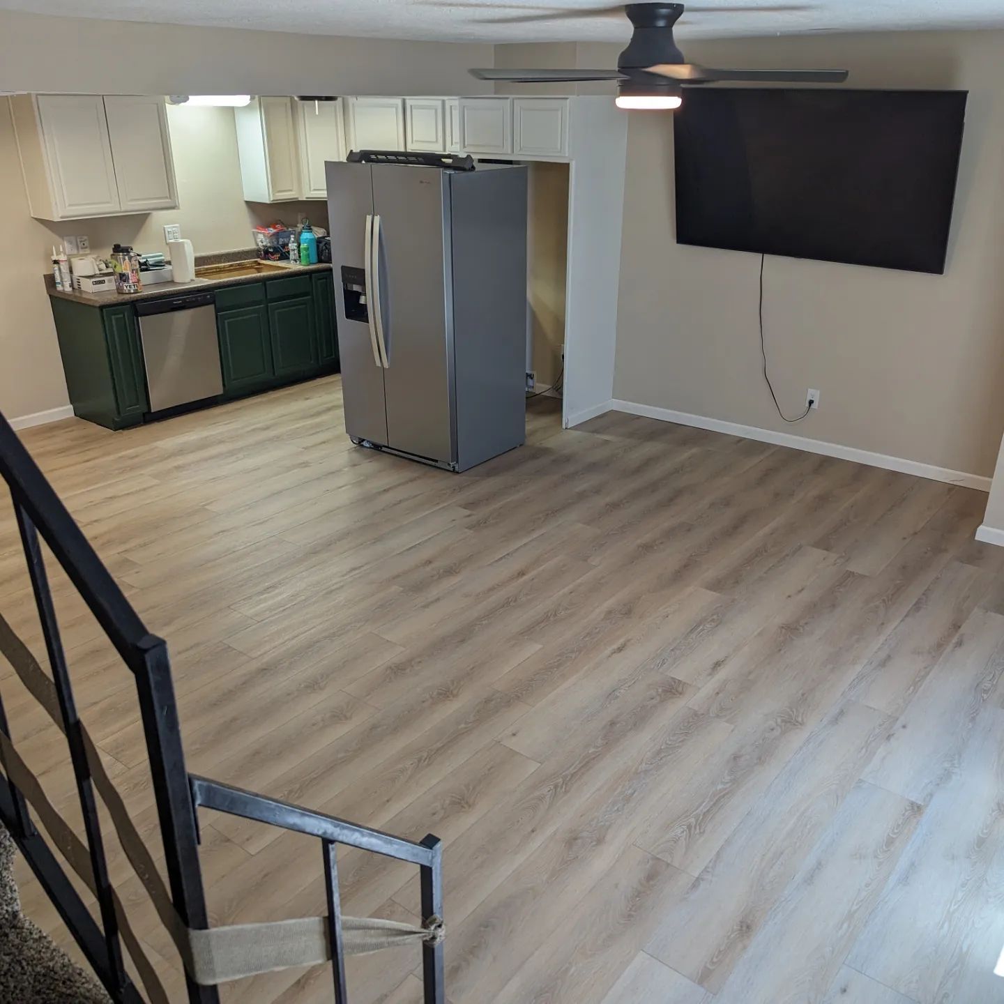 A living room with a refrigerator , television , stairs and a ceiling fan.