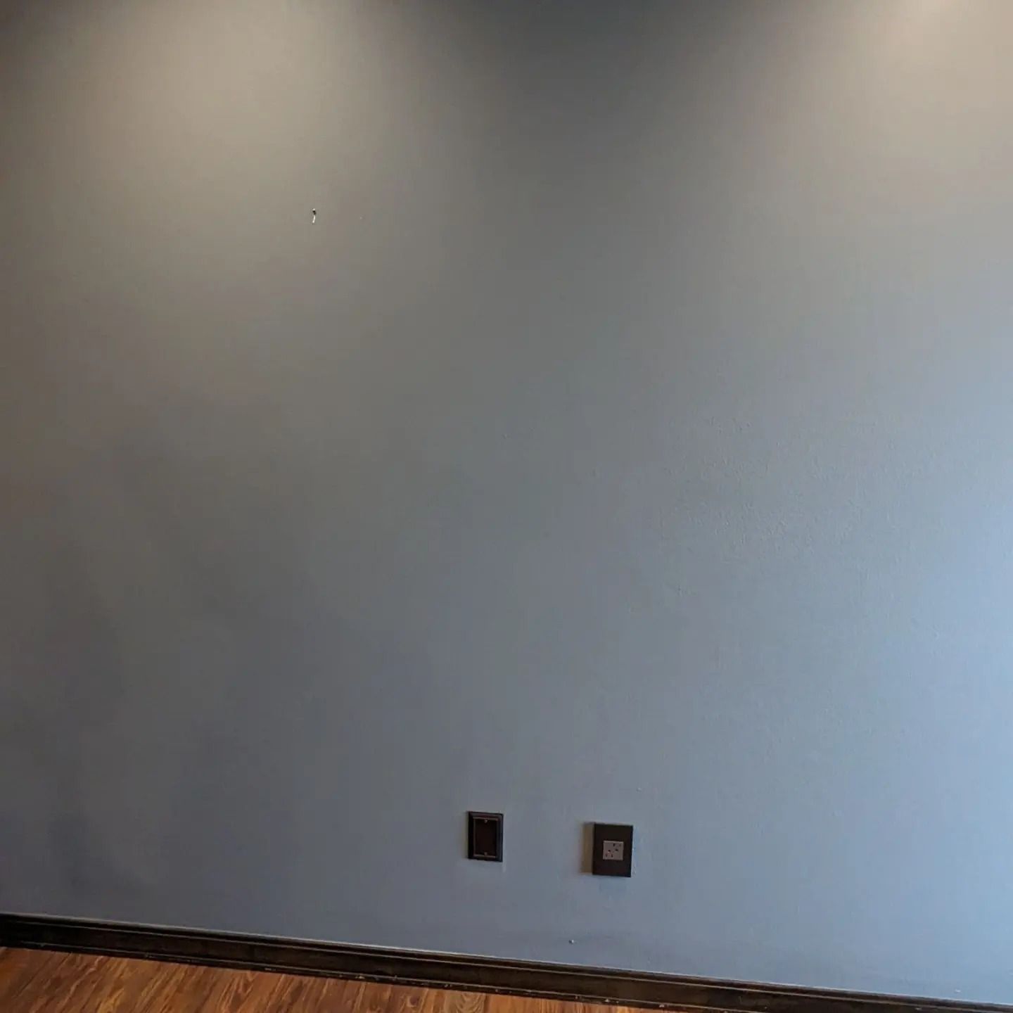 An empty room with a gray wall and wooden floor.