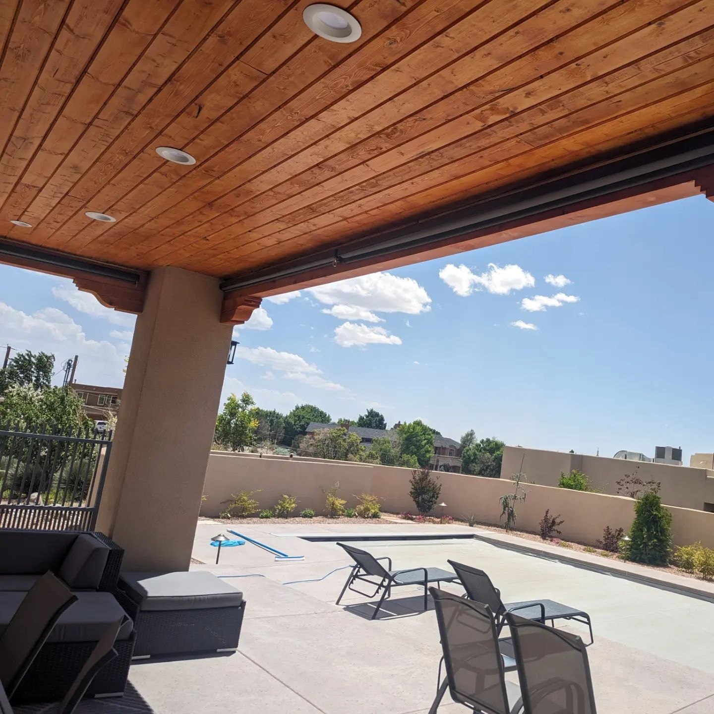 A patio with chairs and a swimming pool under a wooden roof