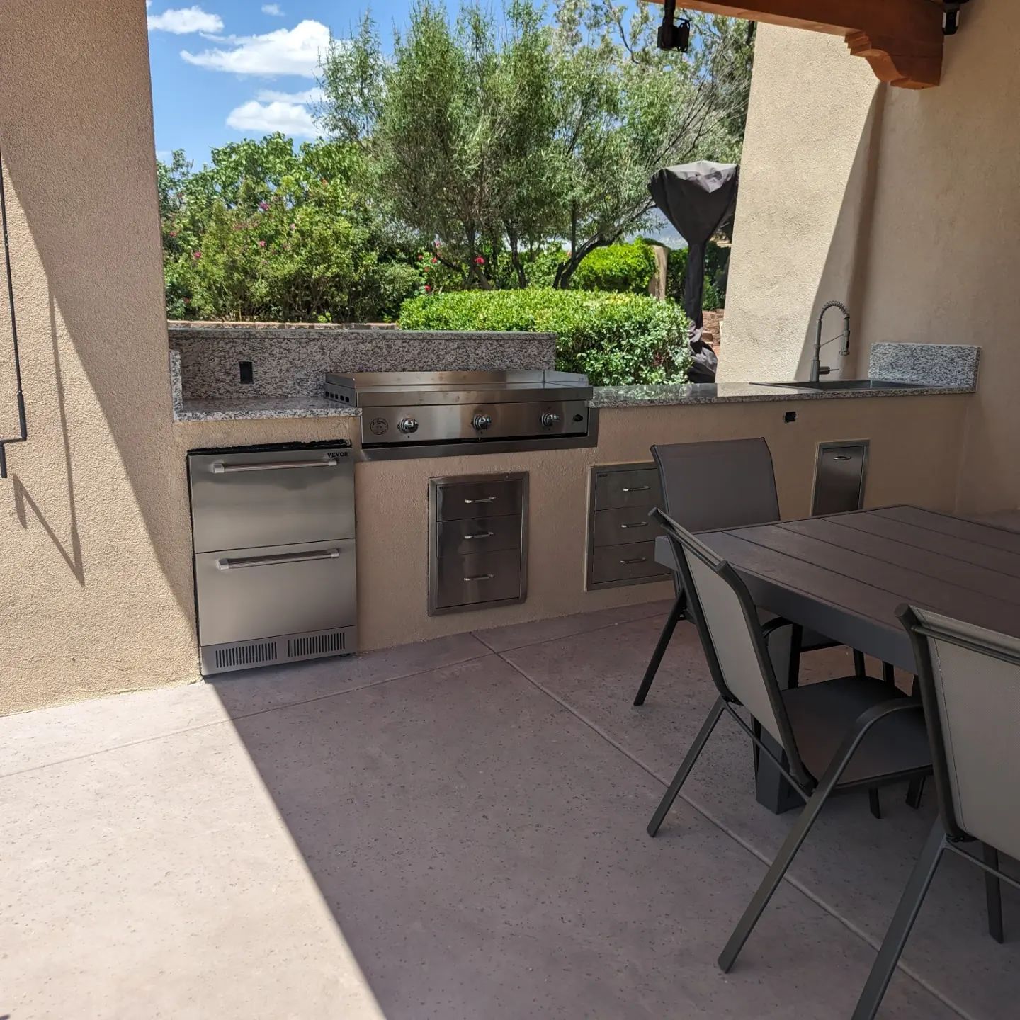 An outdoor kitchen with a table and chairs and a grill