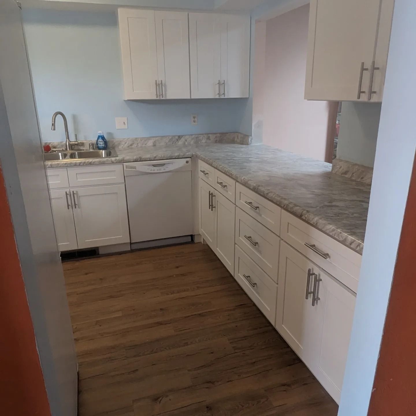 A kitchen with white cabinets , a sink , and a dishwasher.