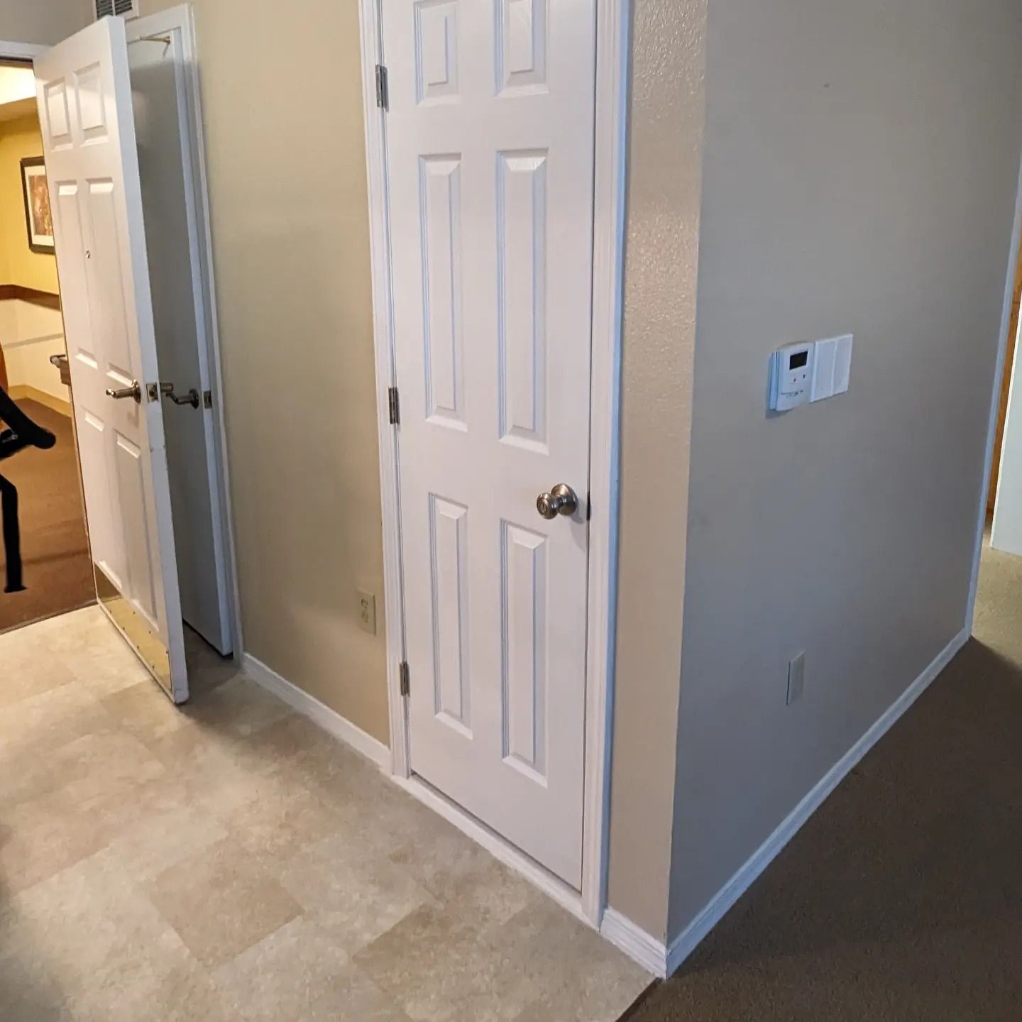 A hallway with a white door and a thermostat on the wall.
