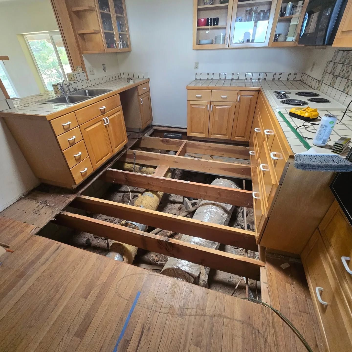 A kitchen with a hole in the floor and wooden cabinets.