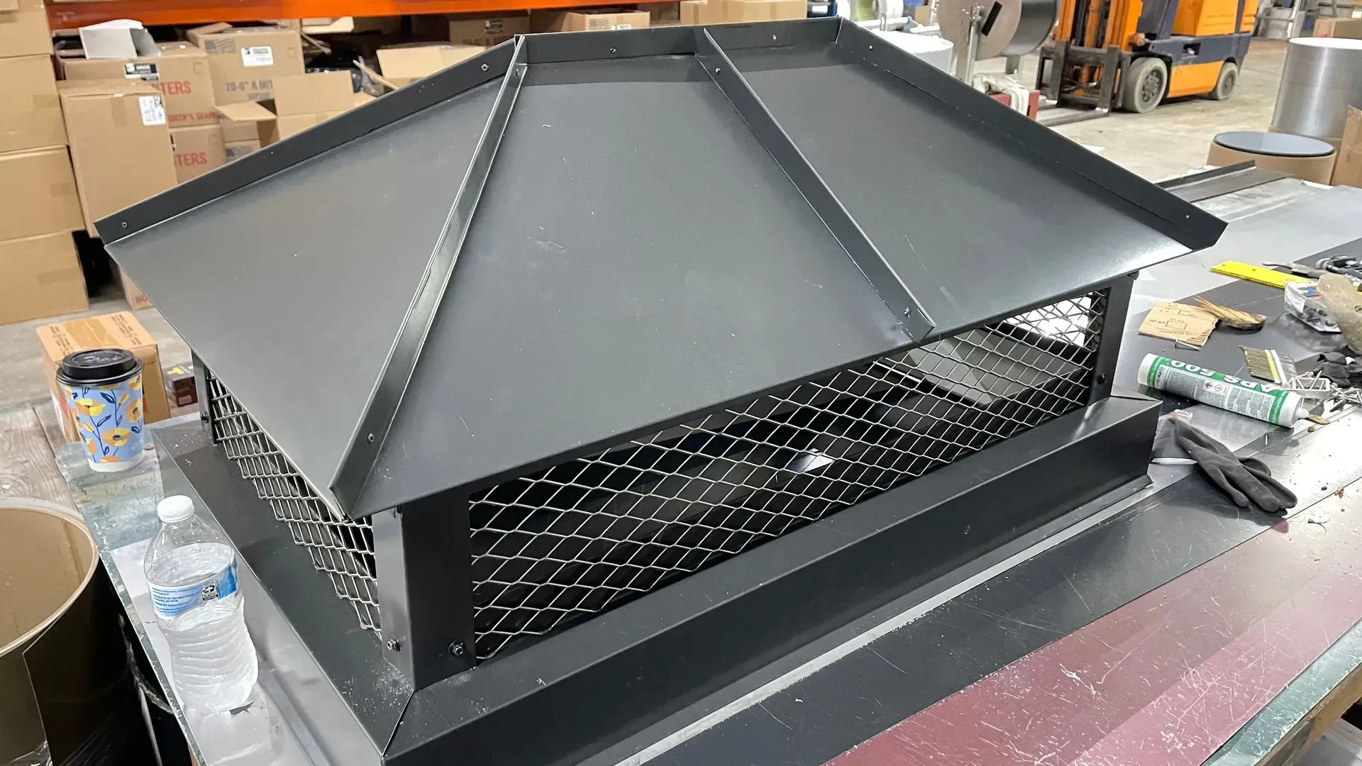 A metal chimney cap is sitting on top of a metal table.