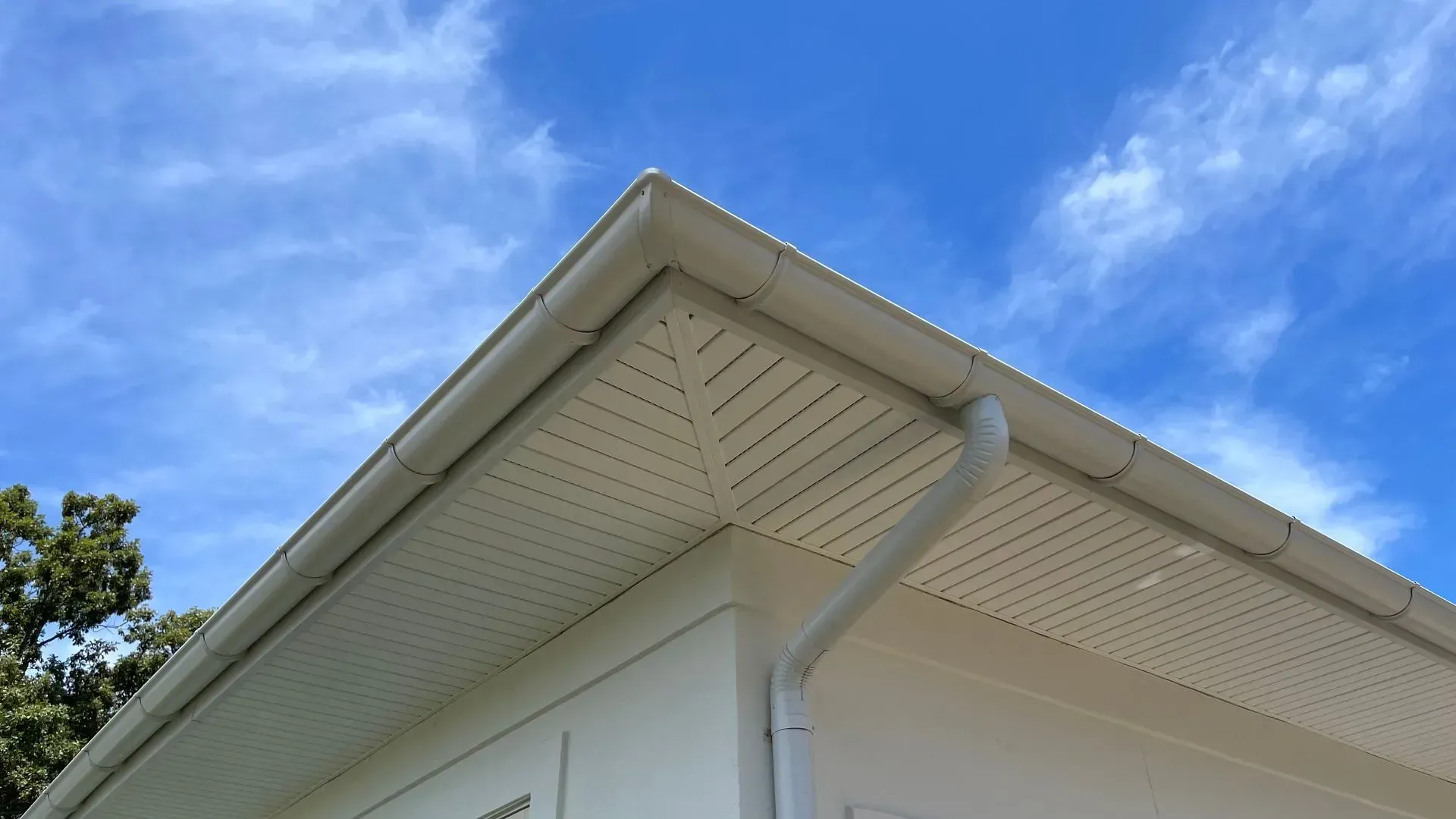 The roof of a white house with a gutter and a blue sky in the background.