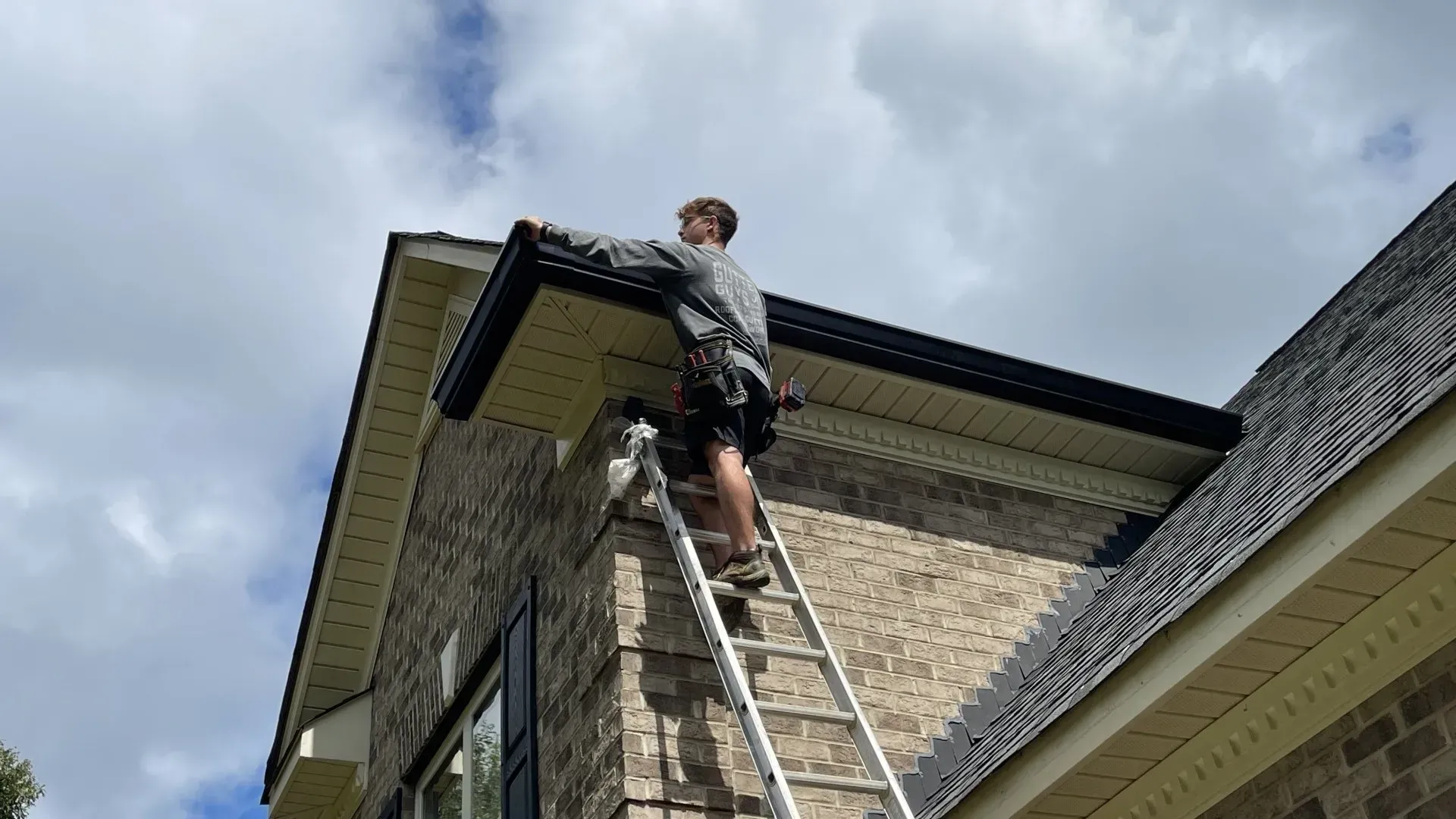 A man is standing on a ladder on the roof of a house.