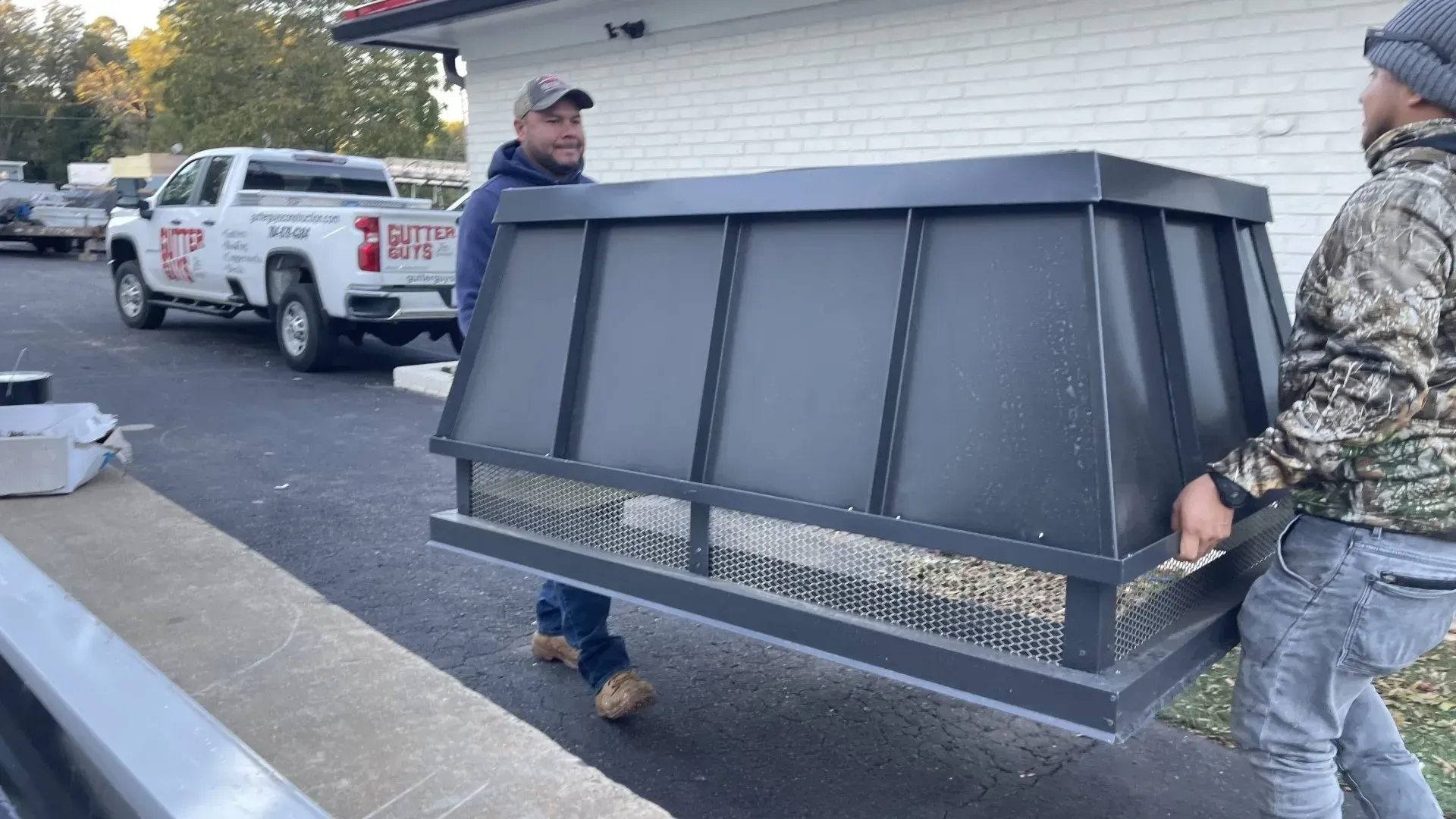 Two men are carrying a large black box in front of a white truck.