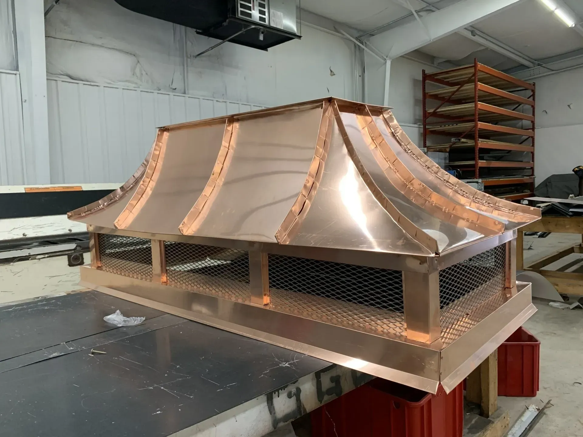 A copper chimney cap is sitting on top of a table in a warehouse.