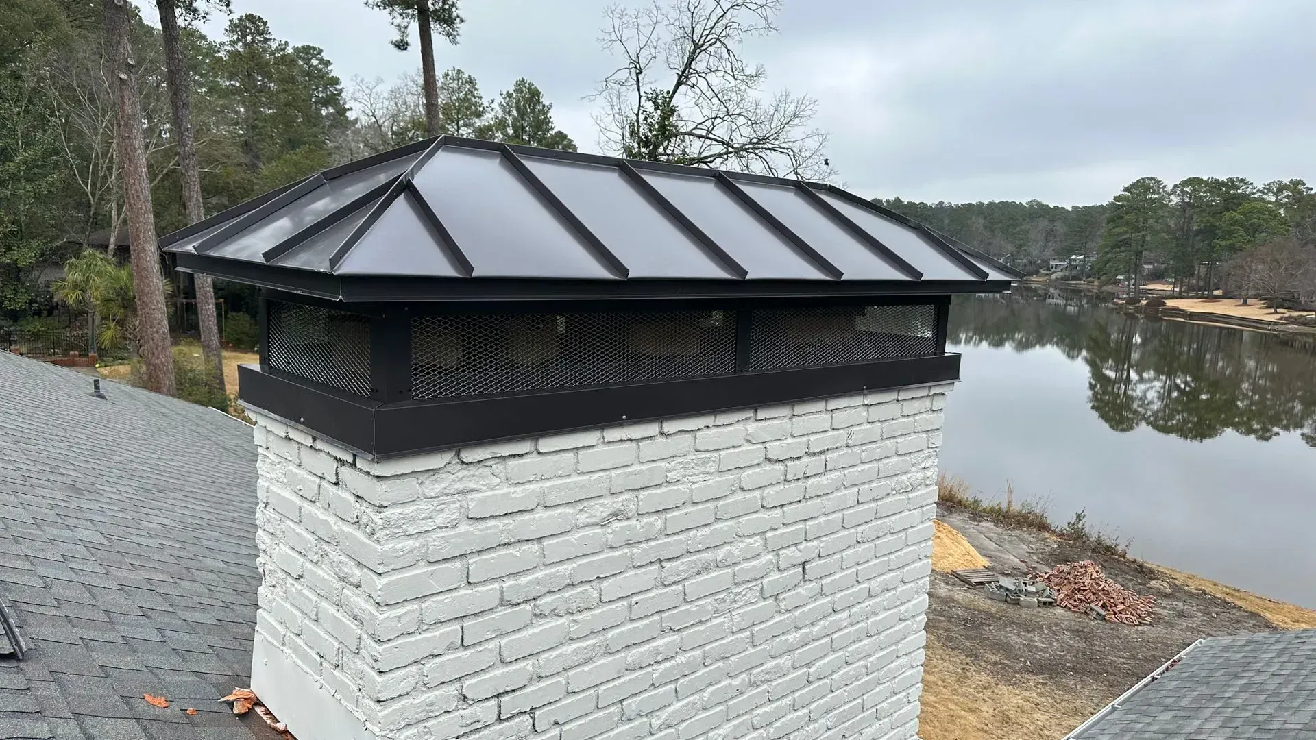 A white brick chimney with a black roof is next to a lake.