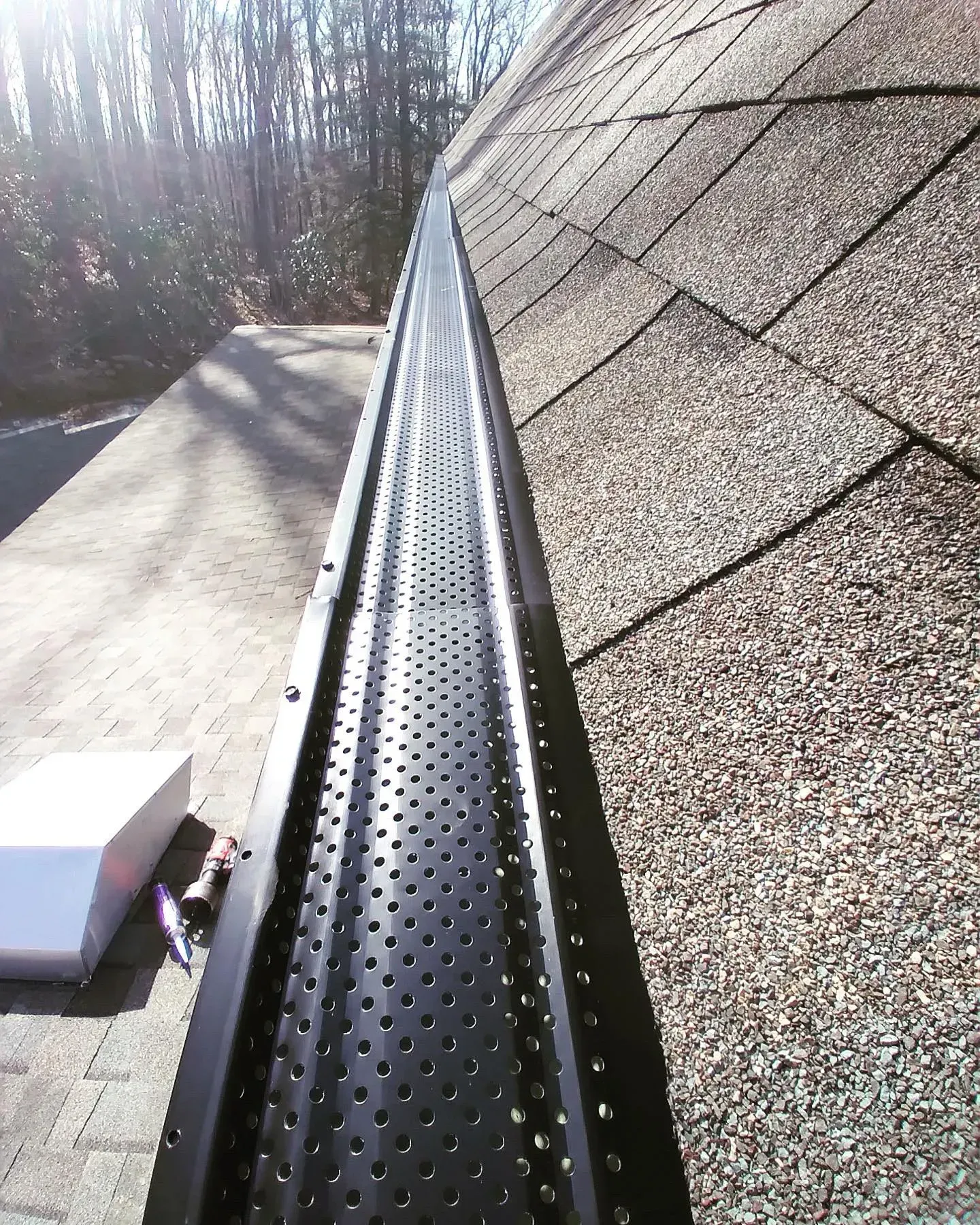 A gutter with holes in it is sitting on top of a roof.