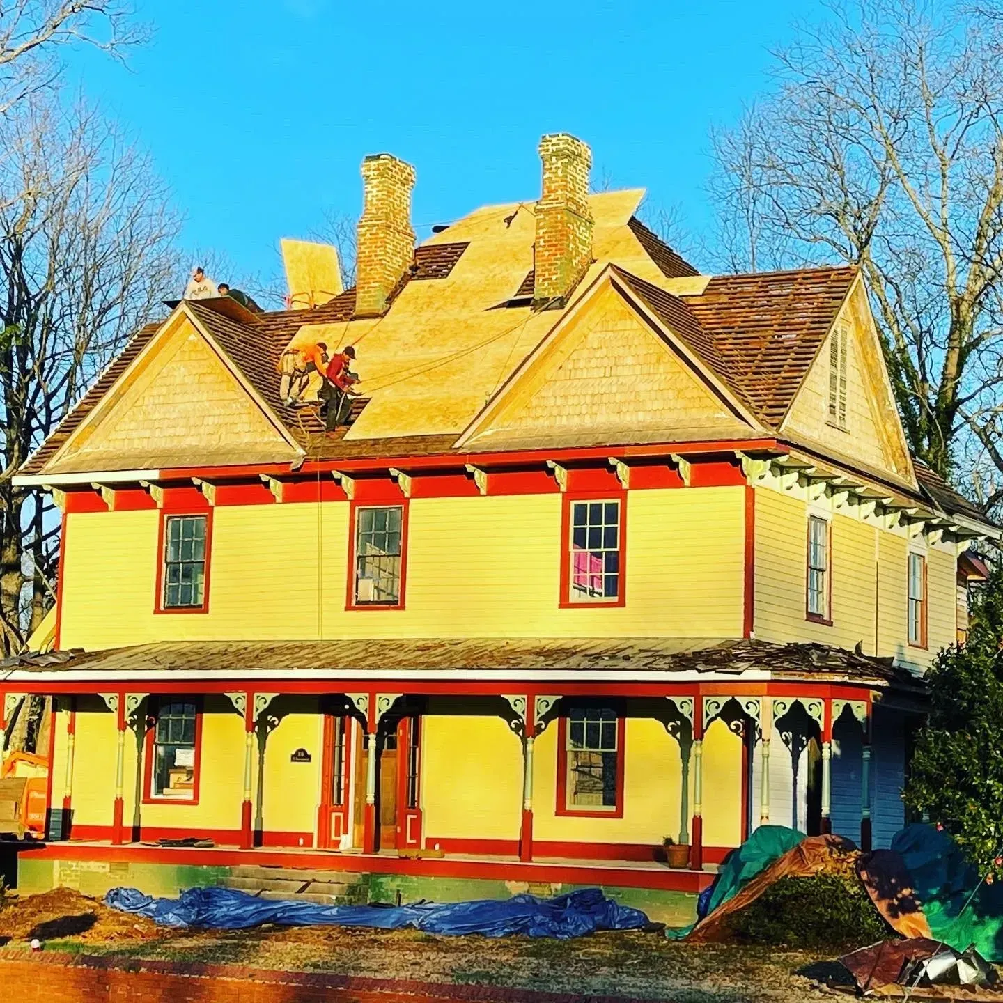 A yellow house with a red trim is being remodeled