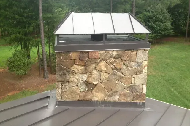 A stone chimney on top of a metal roof