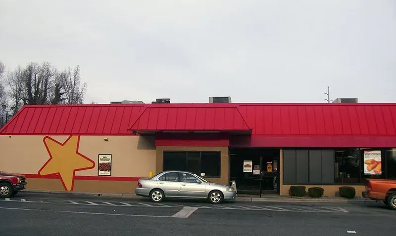 A silver car is parked in front of a fast food restaurant