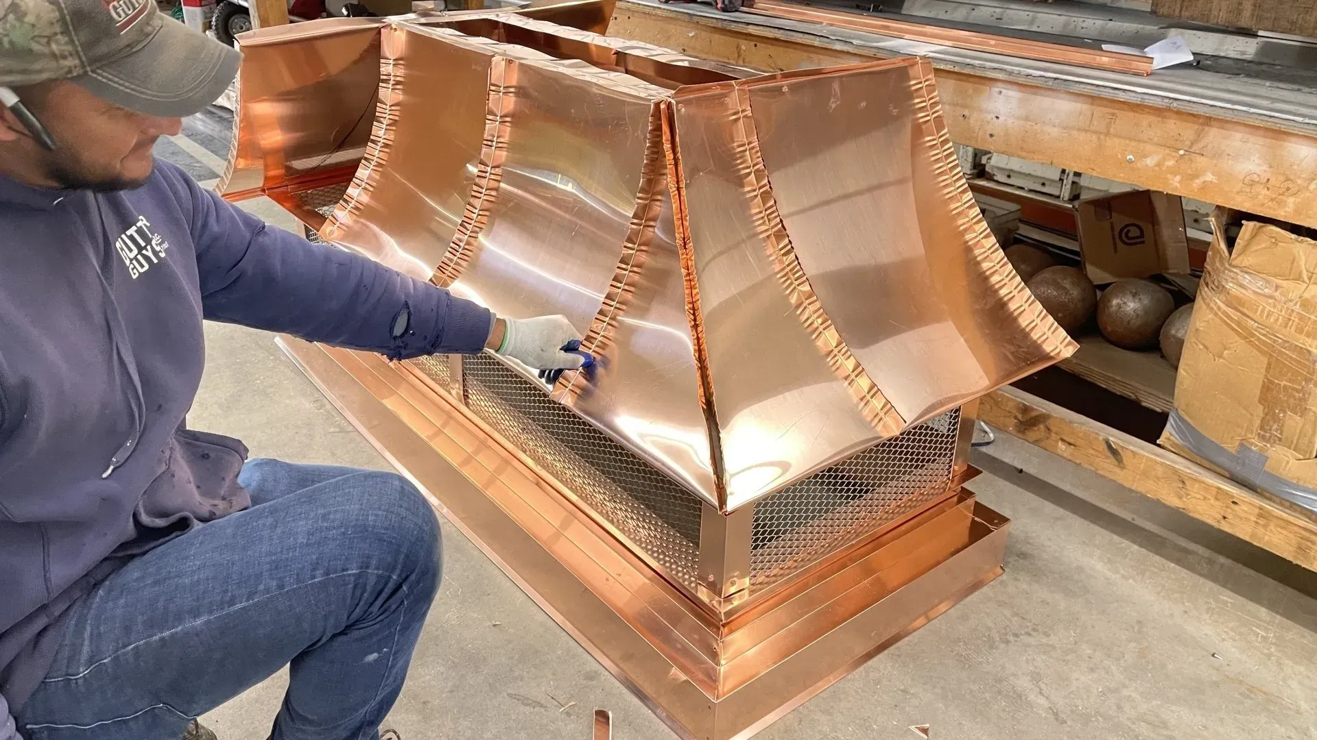 A man is working on a copper hood in a factory.