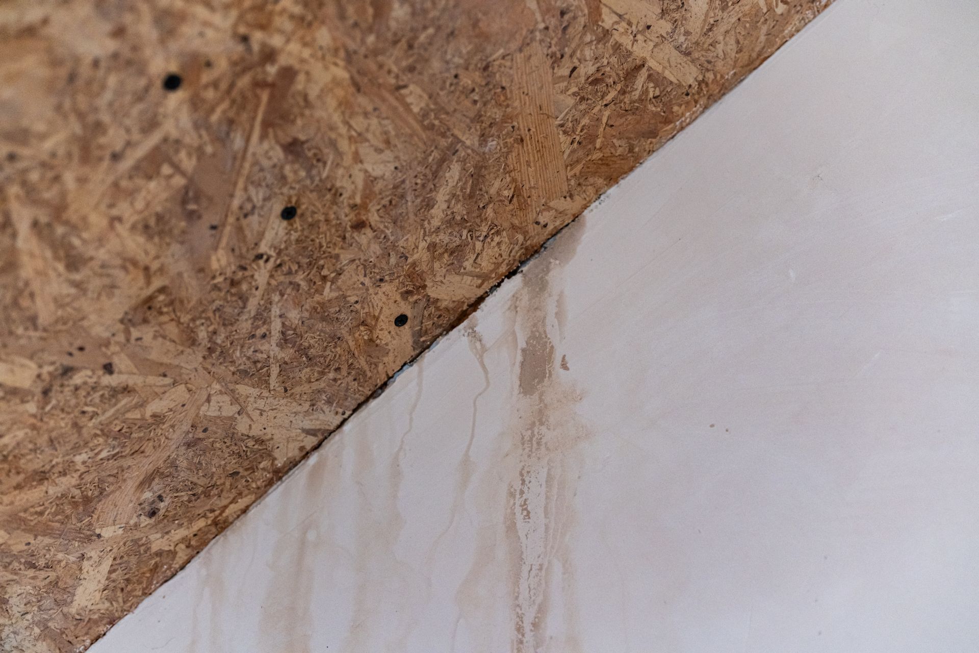 Corner of a wooden OSB panel and white wall with water stains