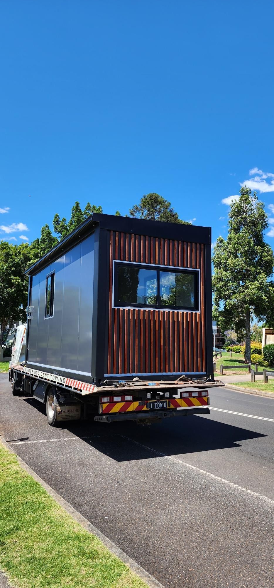 A Truck Is Carrying a Small House Down a Street — Alternative Modular Home In Toowoomba City, QLD
