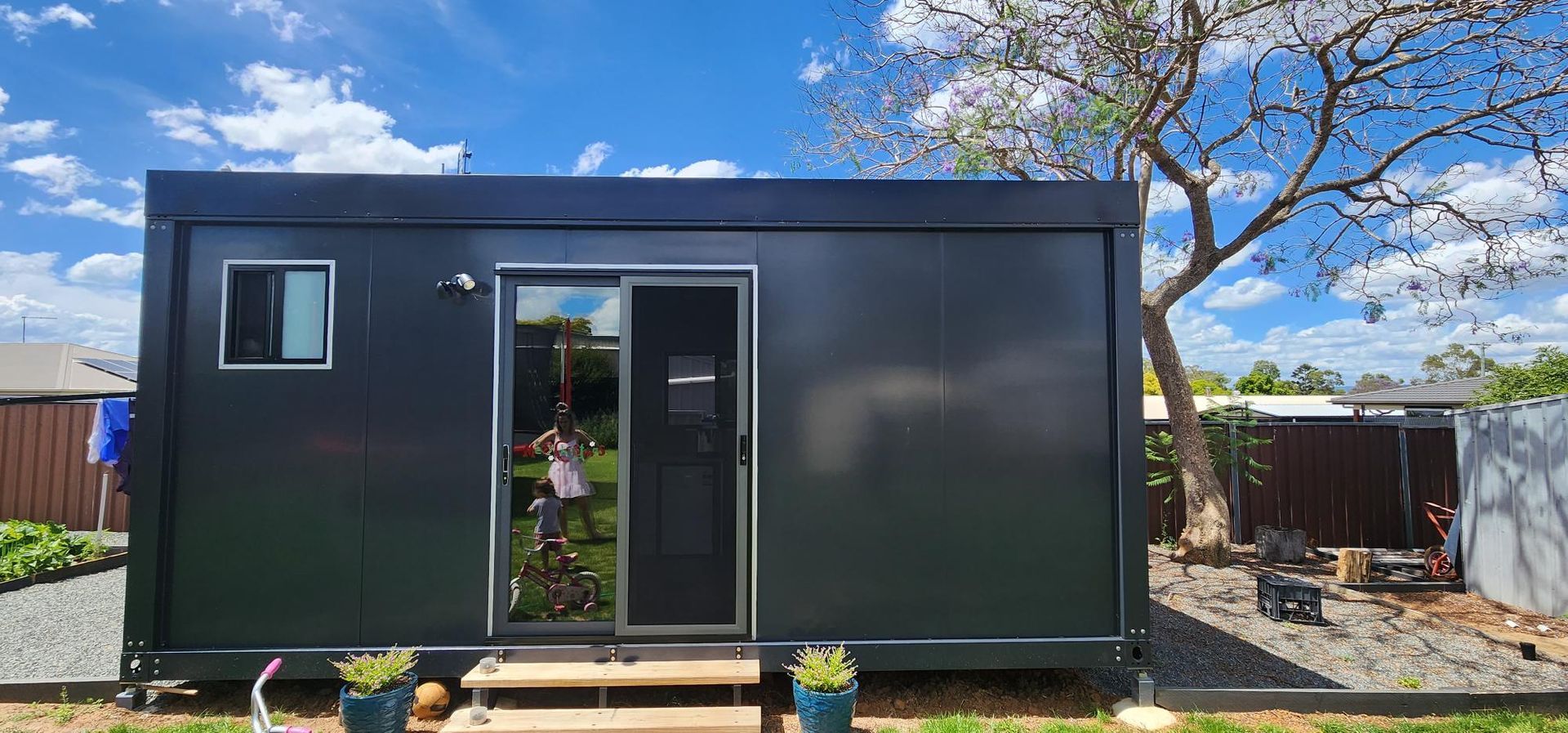A Small Black House Is Sitting in The Middle of A Yard Next to A Tree — Alternative Modular Home In Toowoomba City, QLD