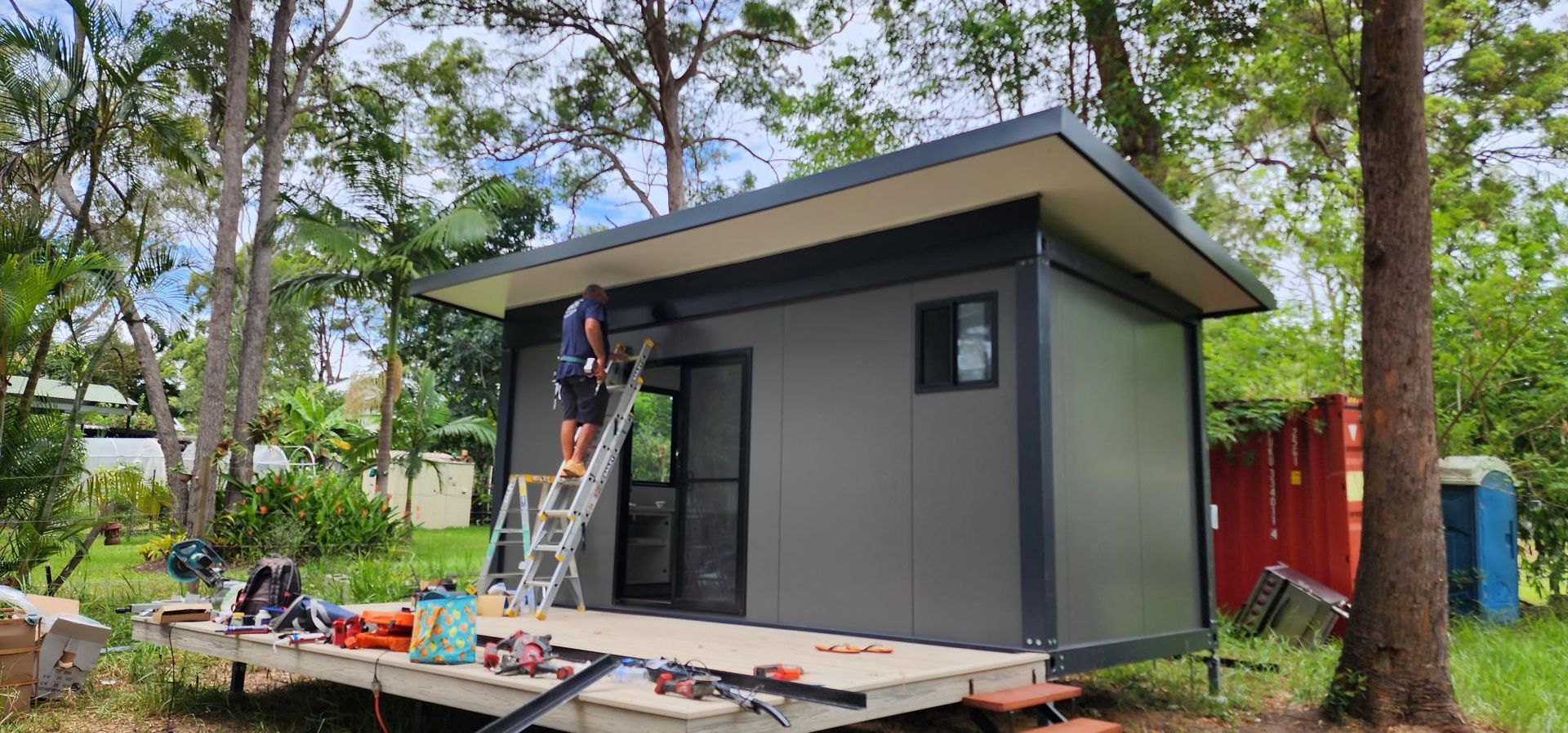 A Man Is Standing on A Ladder in Front of A Small House — Alternative Modular Home In Toowoomba City, QLD