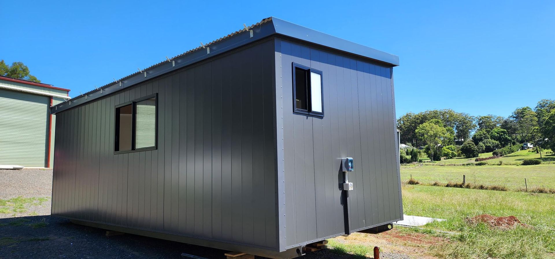 A Small Black Building Is Sitting in The Middle of A Grassy Field — Alternative Modular Home In Toowoomba City, QLD